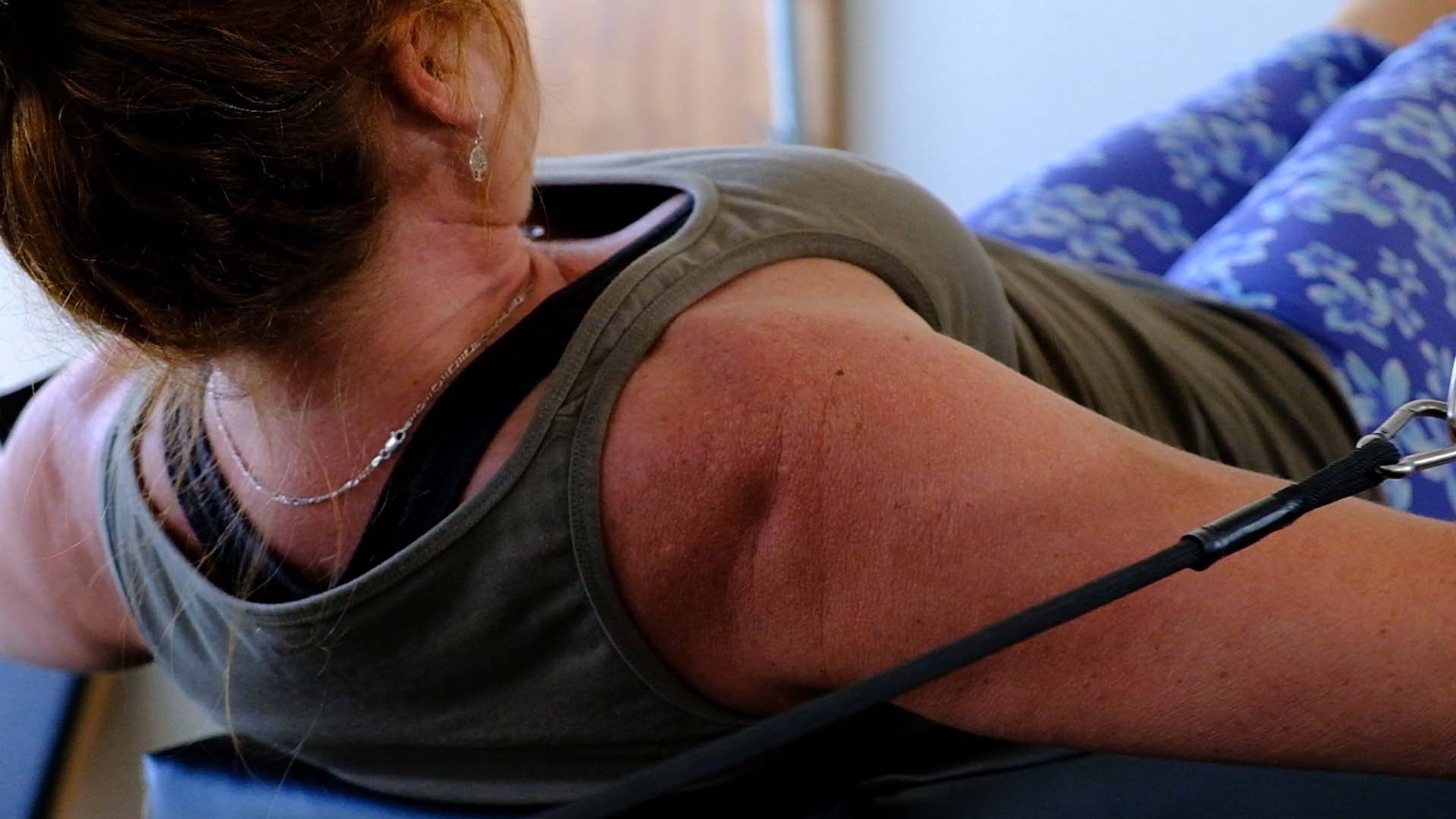 Woman lying on a reformer with a spring strap across her shoulder