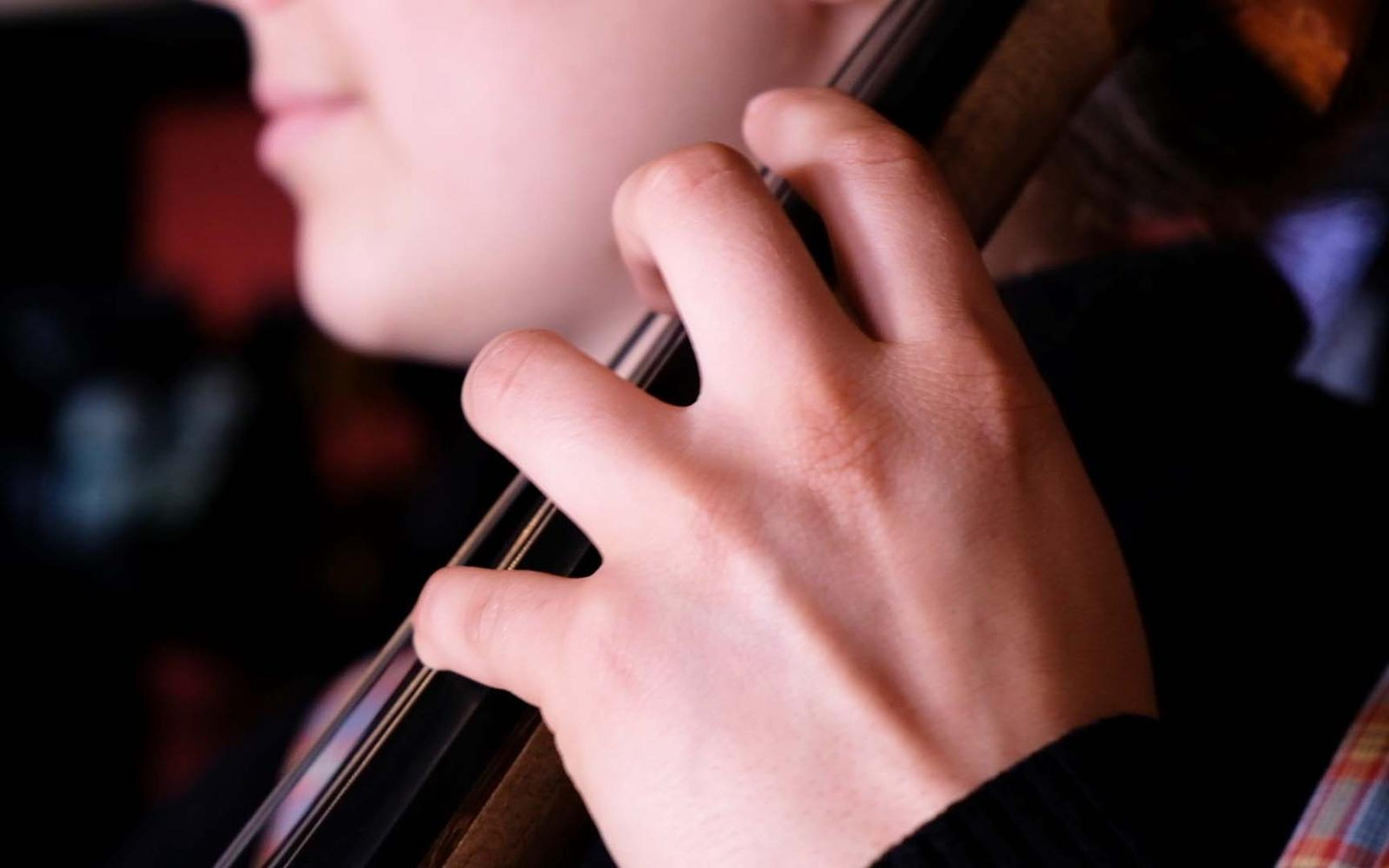 Hand pressed on the strings of a large string instrument with a lower face just visible in soft focus
