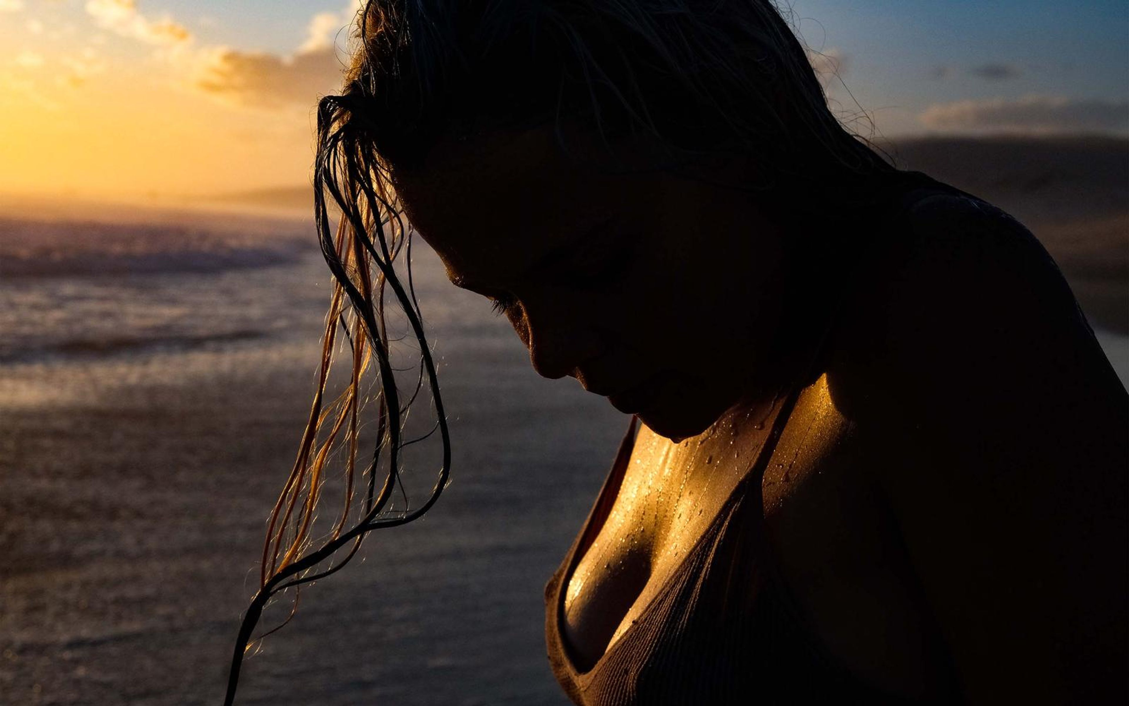 Dark silhouette of a woman bowing her head with long wet hair hanging, orange and blue dusk sky