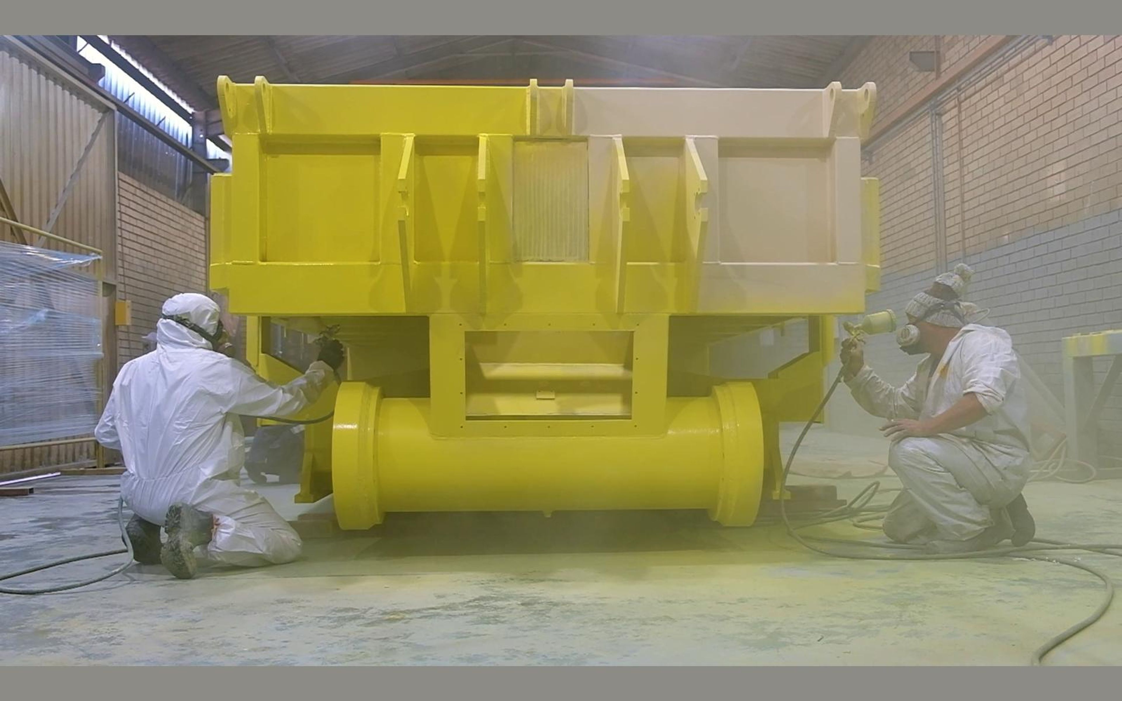 Yellow painted steel component with painters working beside it