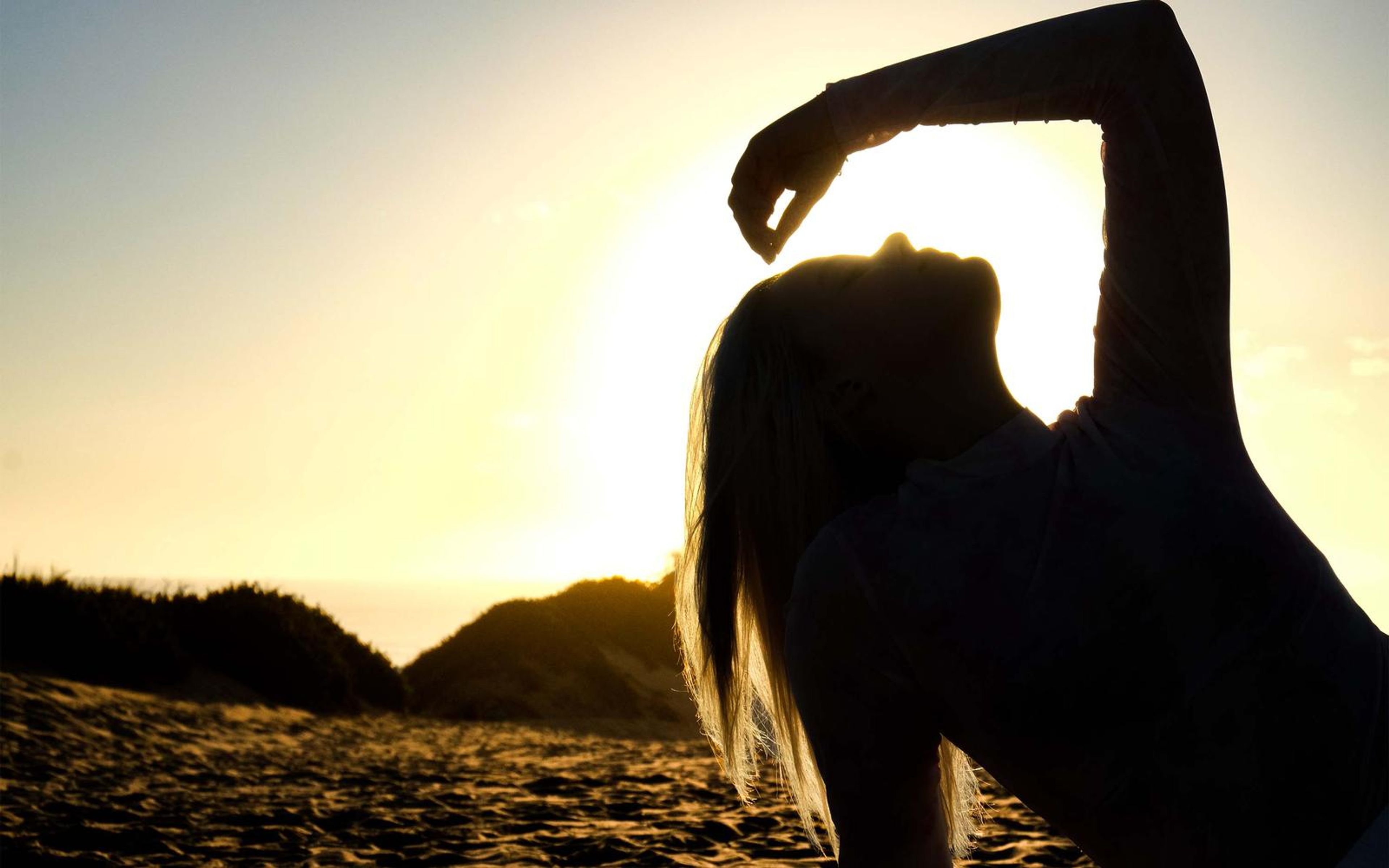 Silhouette of a woman with one arm arched over her head against the sunset