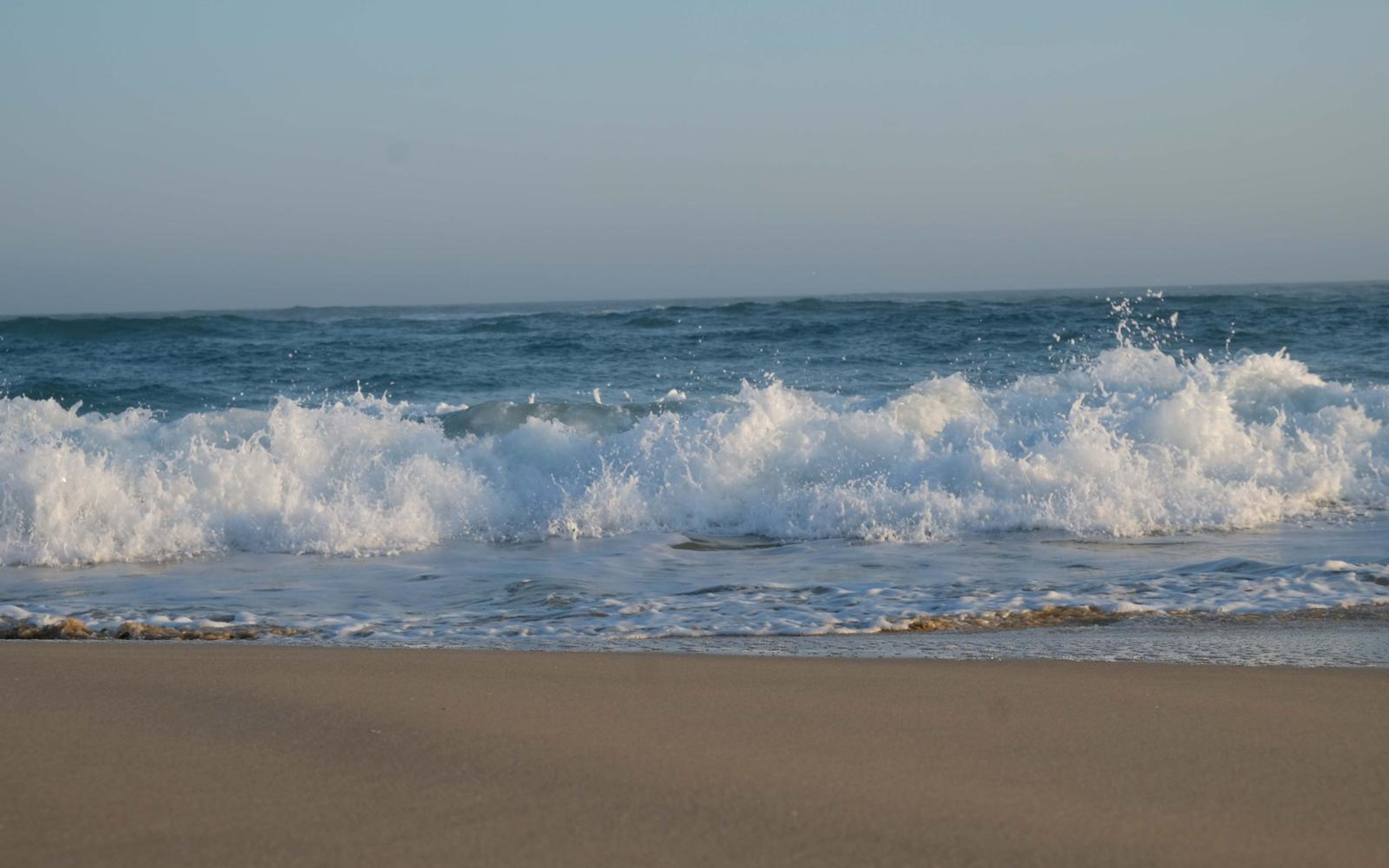 Line of waves breaking along the shore under a hazy sky