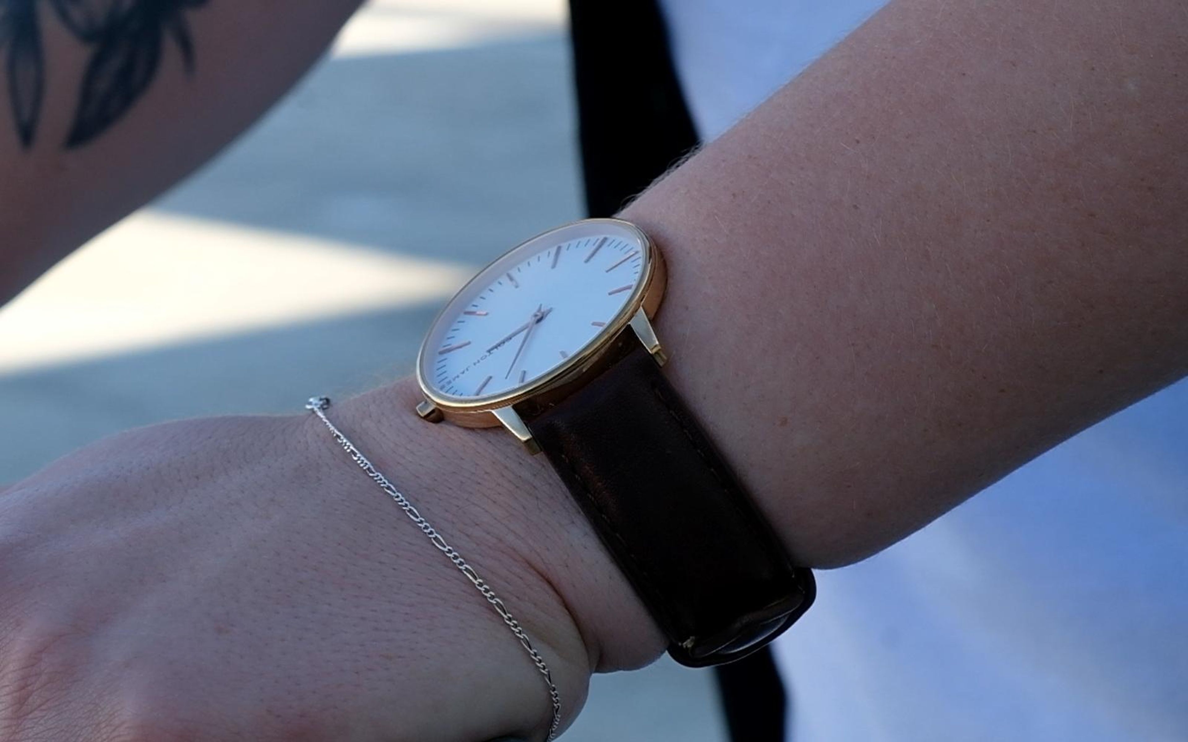 Close view of a wrist with a round white-faced watch on a dark brown leather strap and a fine silver bracelet