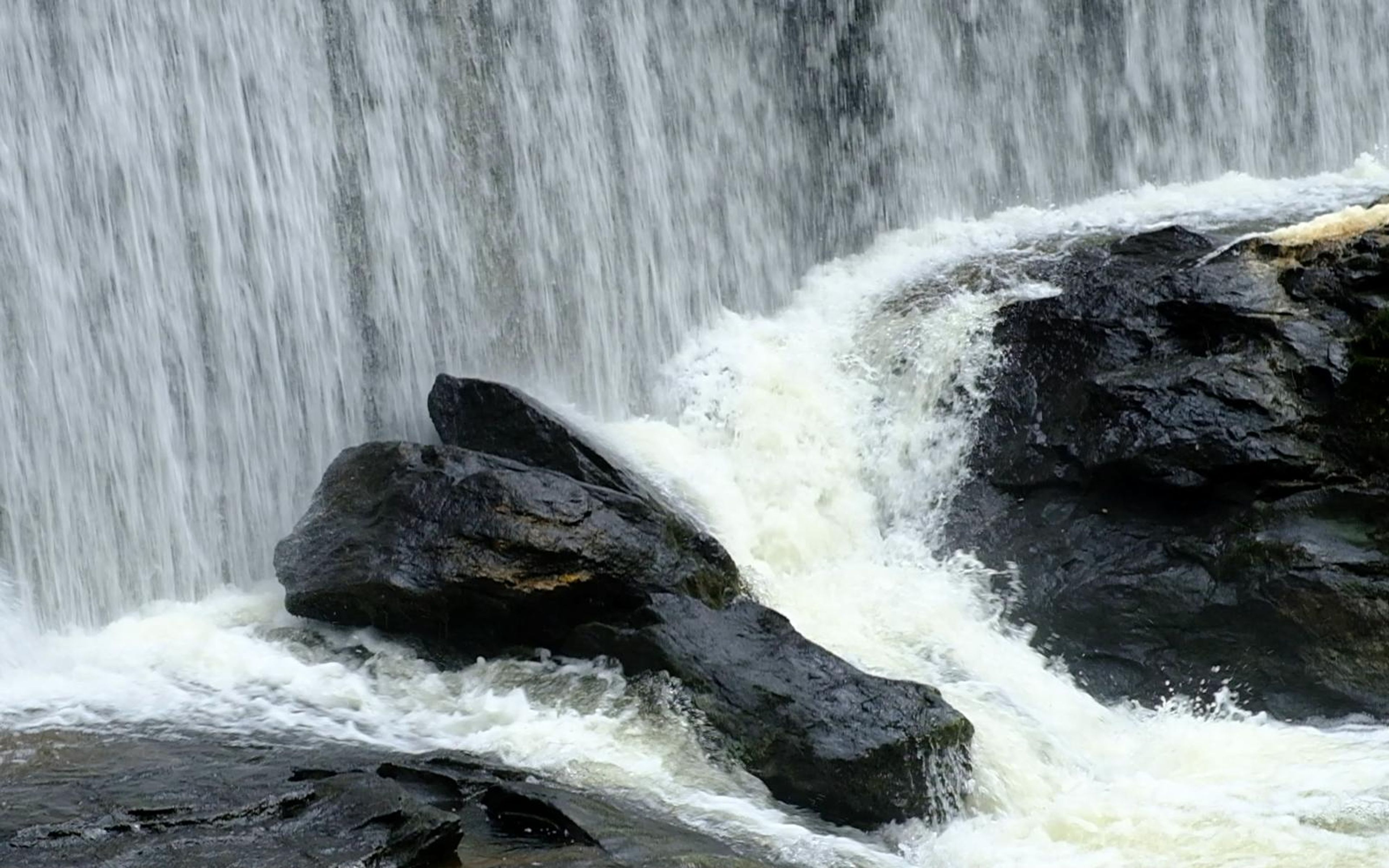 Water pouring around two black boulders into a churning white pool at the base of the falls