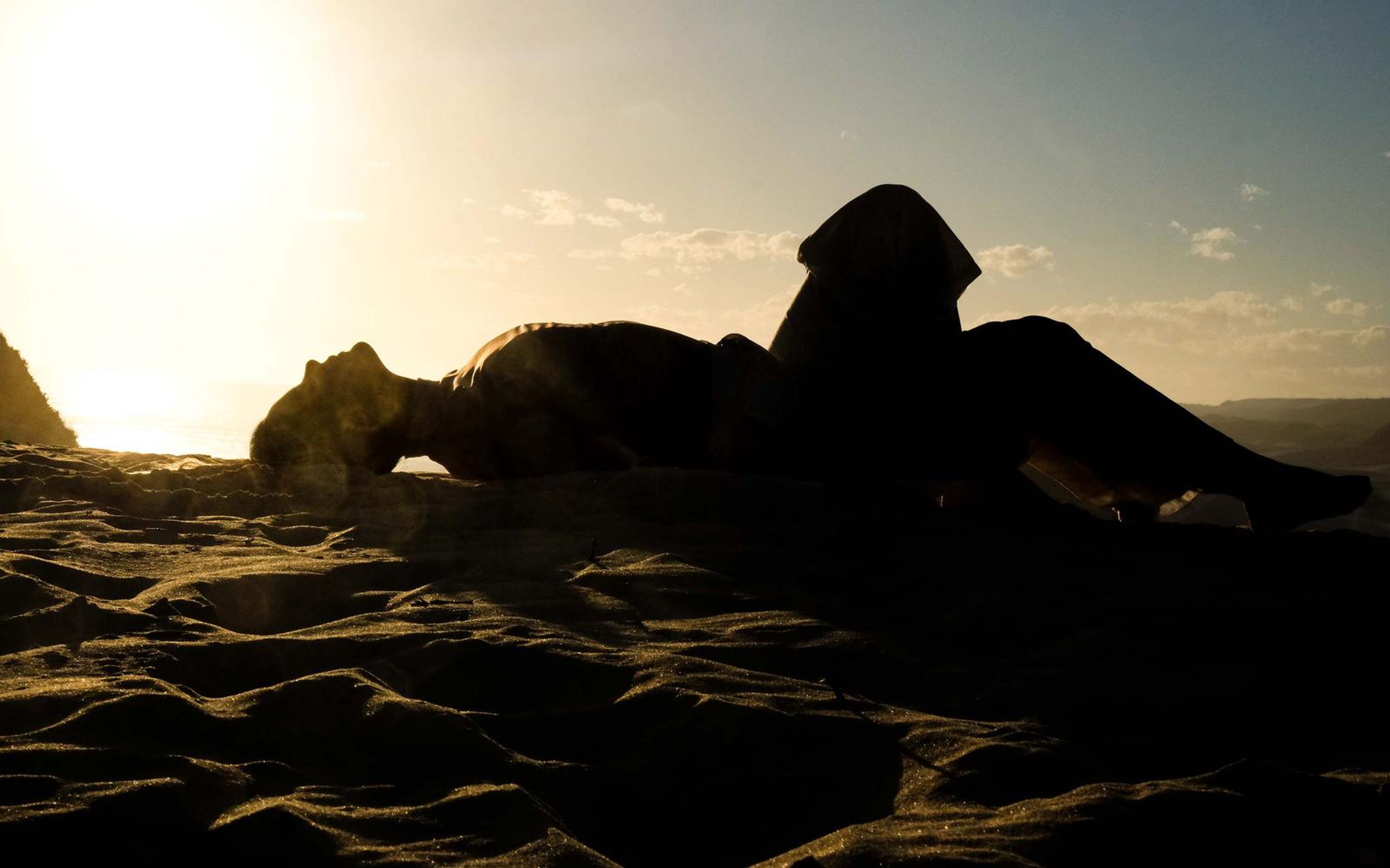 Dark silhouette of a woman lying on a sand ridge against a bright sky