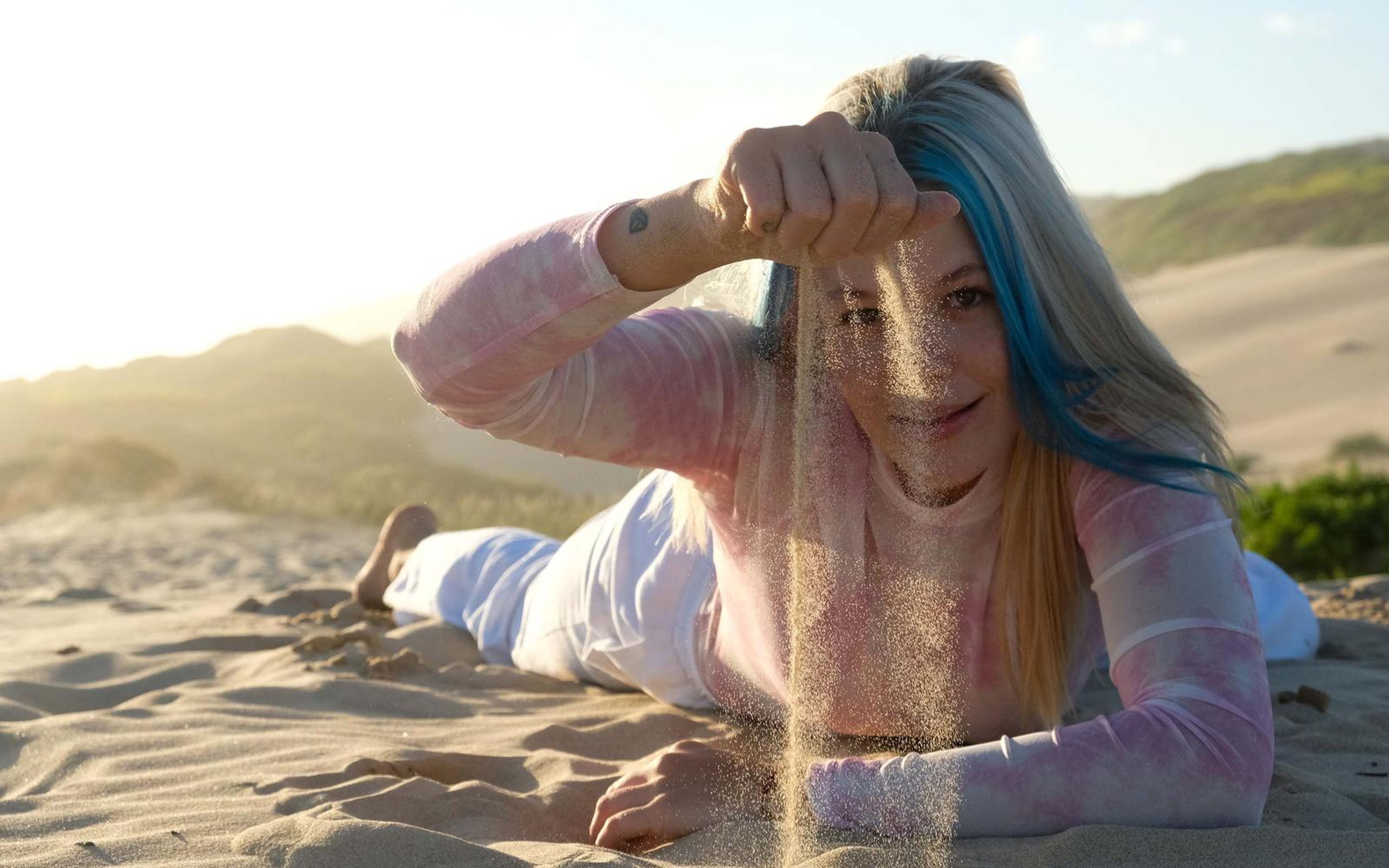 Woman lying on the sand with sand pouring through her fingers over her face