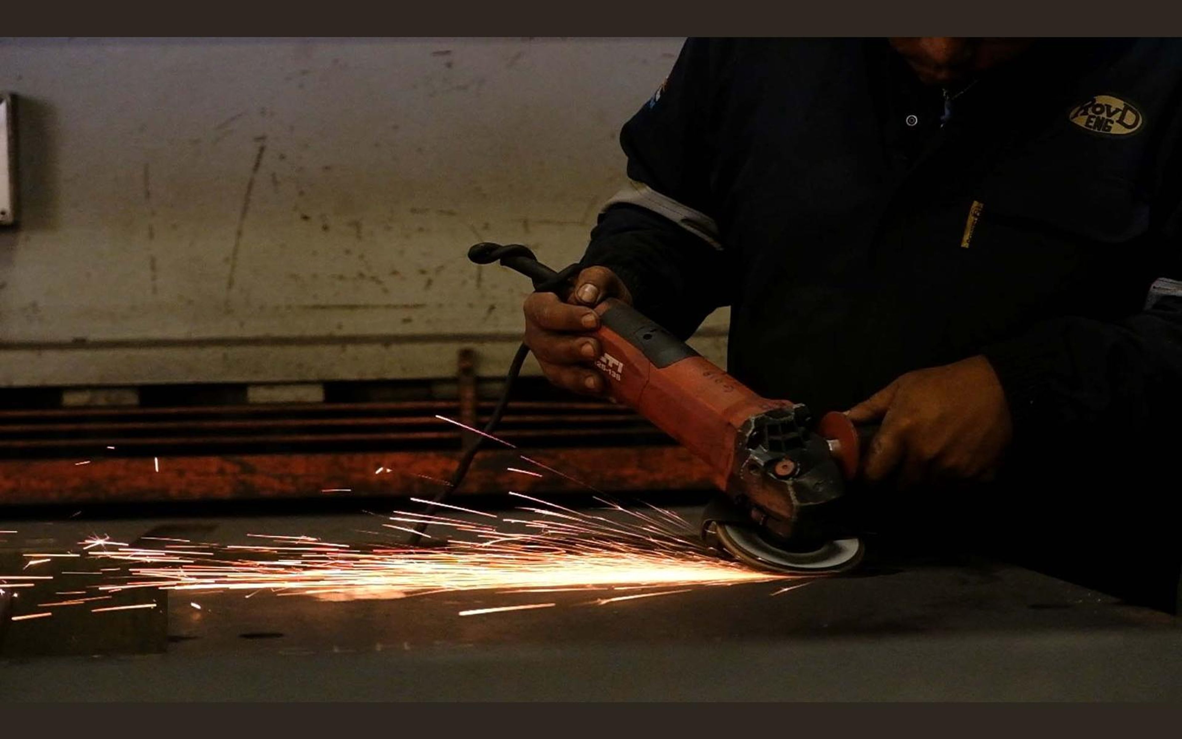 Fabricator grinding a steel edge with orange sparks