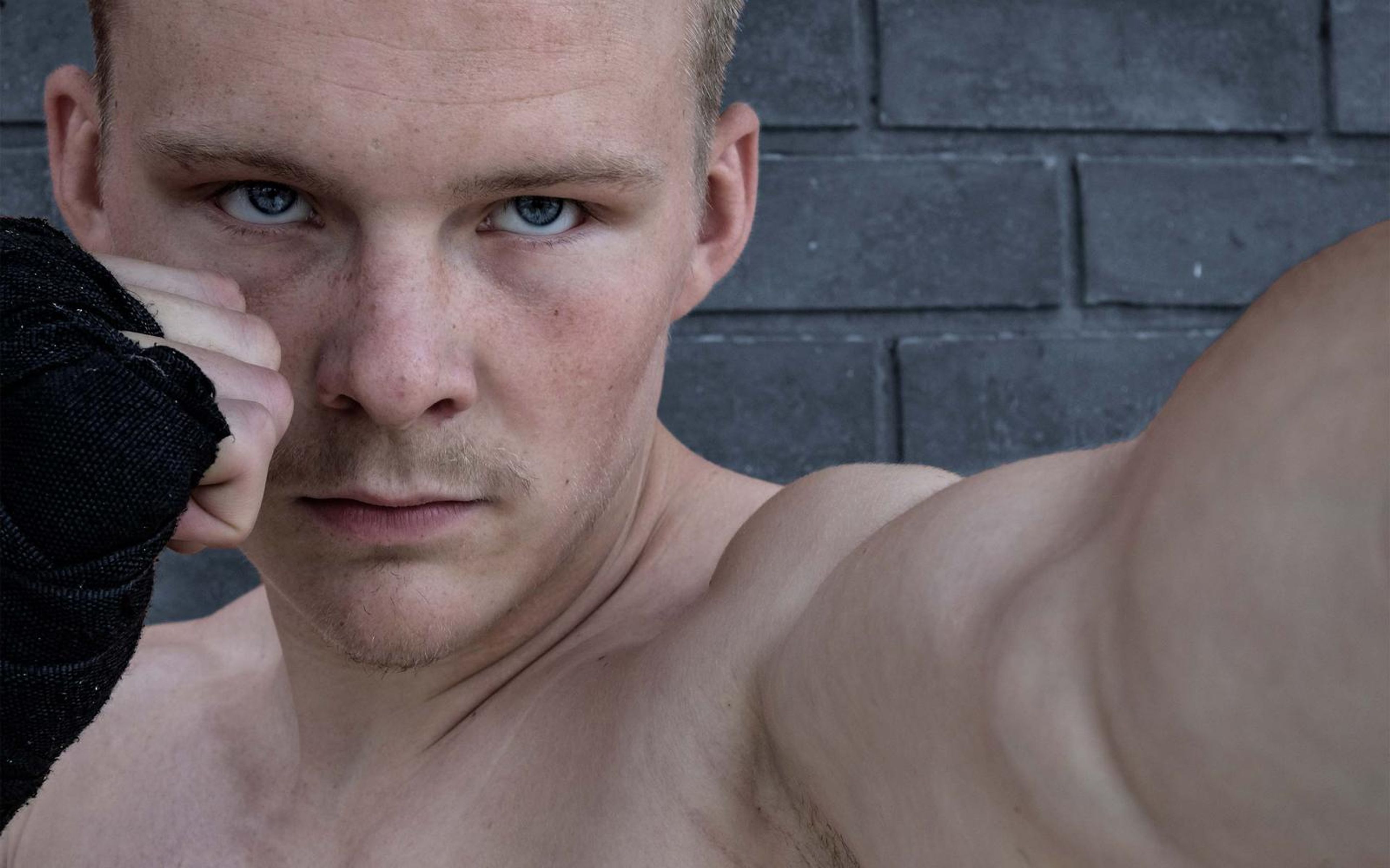 Close-up of the fighter's stare over a raised fist against a dark grey brick wall