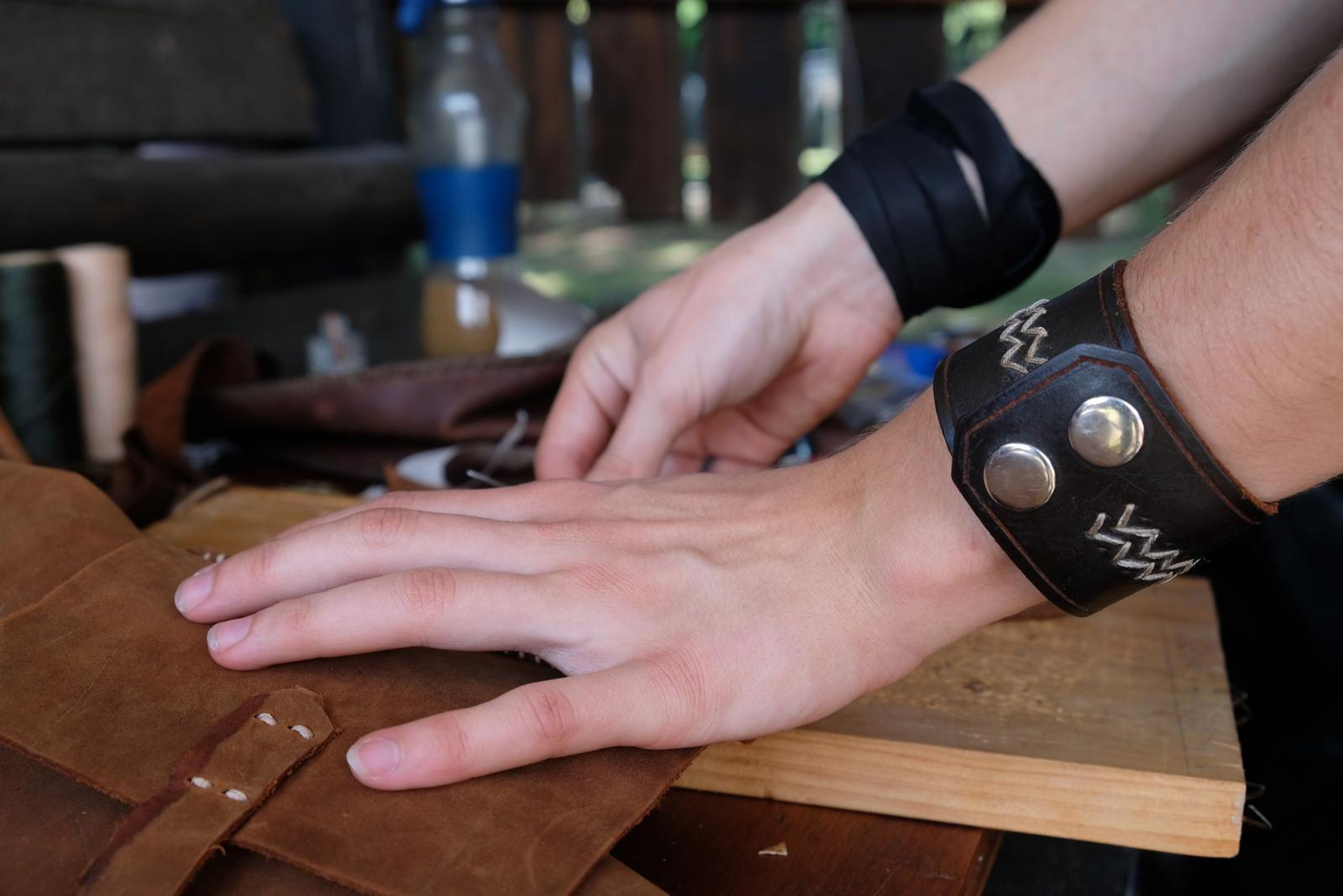 Hand resting on tan leather beside a black leather cuff with white zigzag stitching