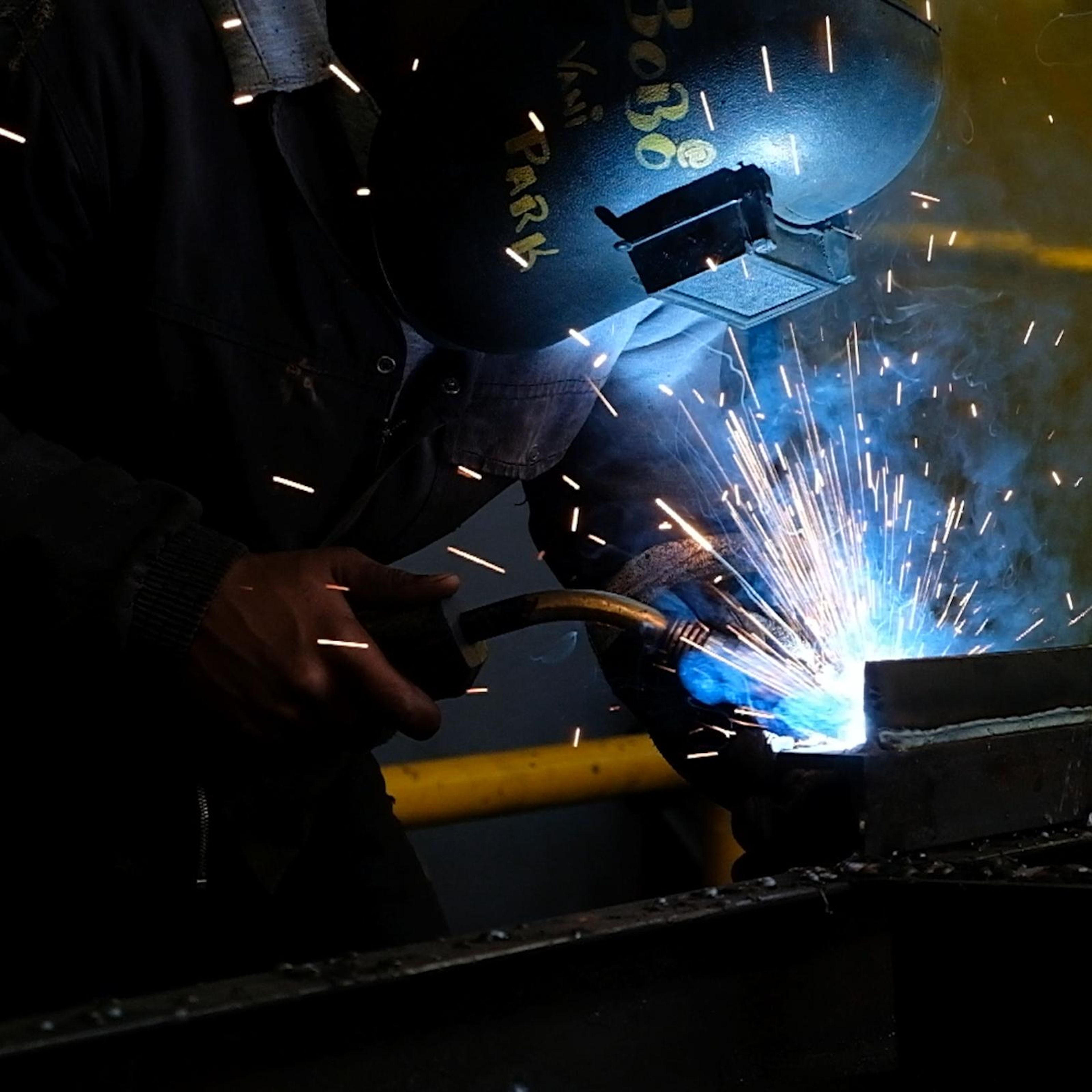 Square crop of a welder in a helmet with sparks flying