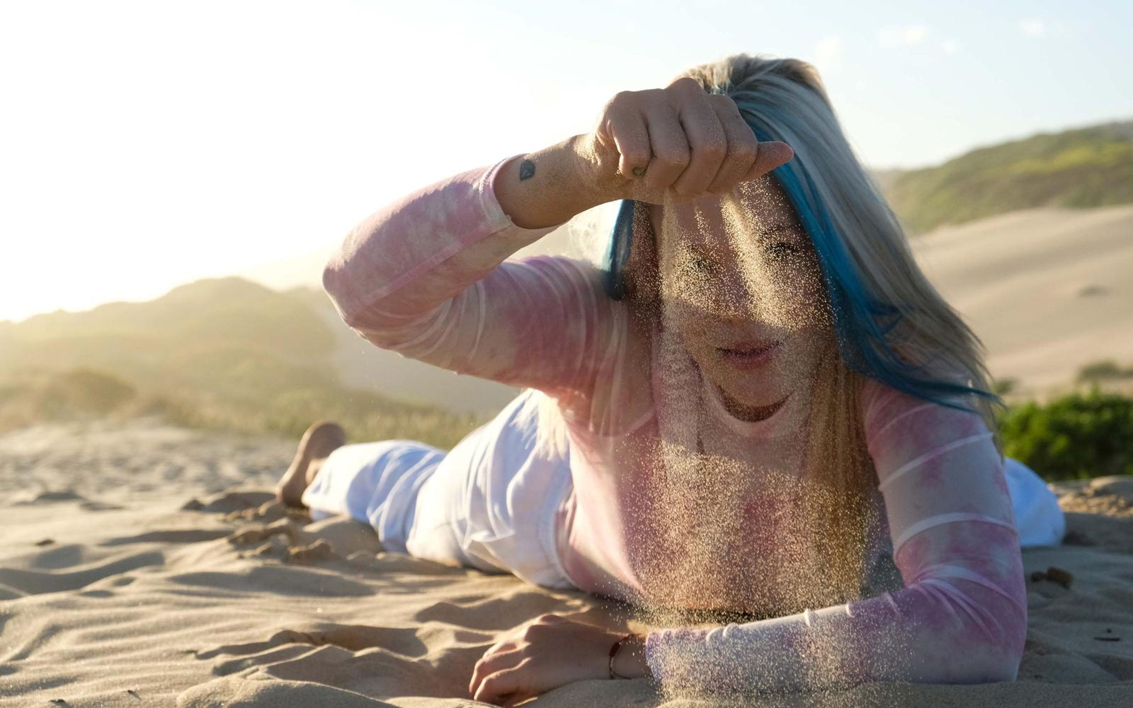 Woman lying on the sand letting sand run through her fingers in front of her face
