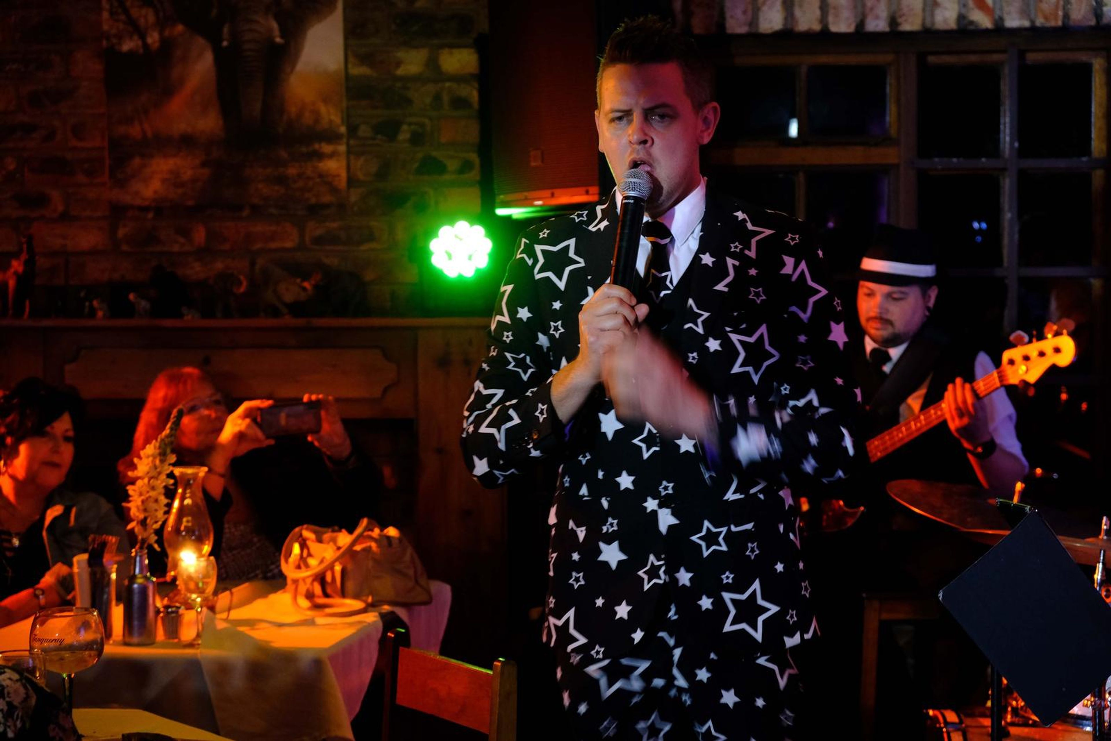 Singer in a star-patterned suit holding the microphone in front of the band
