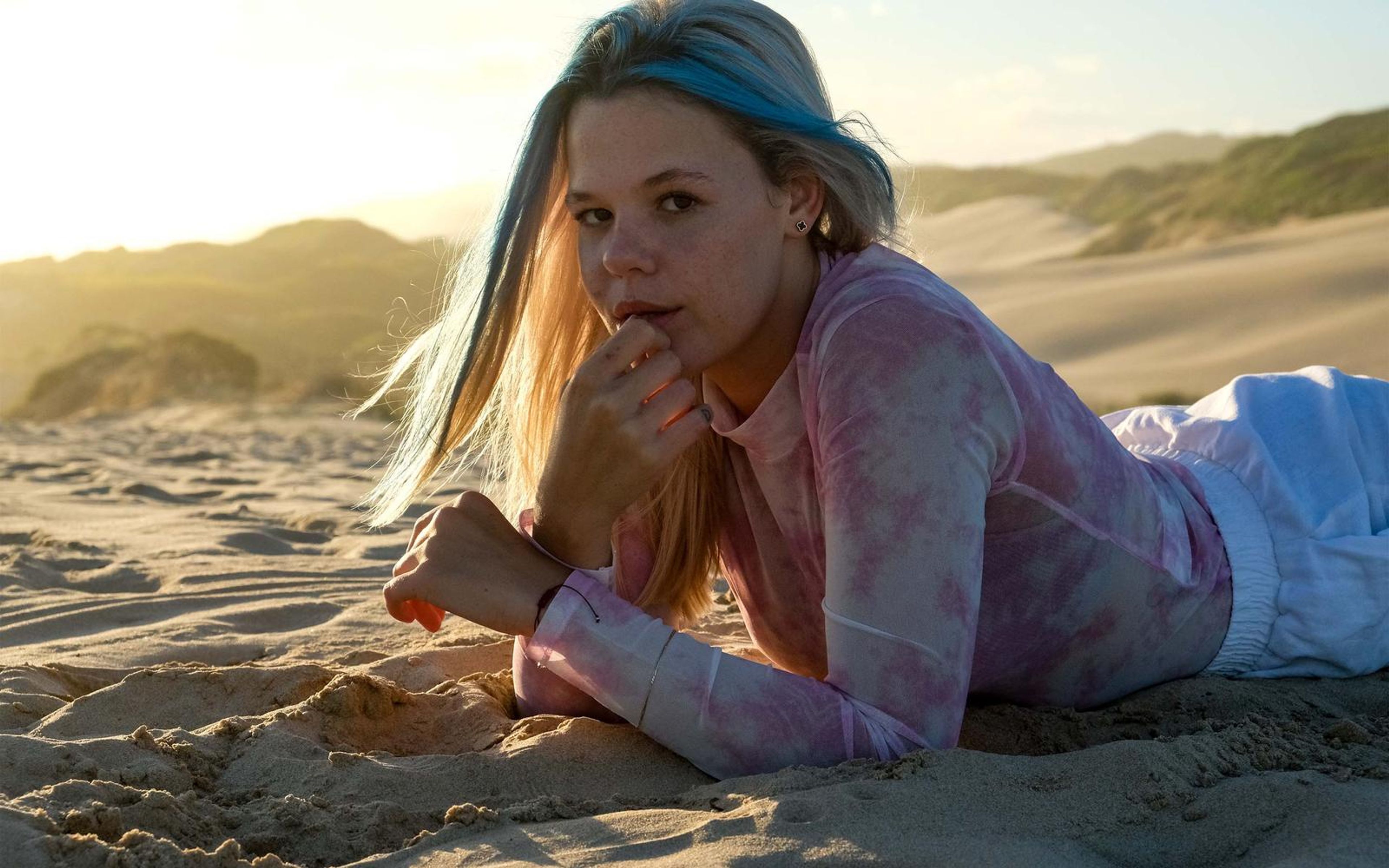 Woman lying on the sand with a hand at her chin and a calm direct look