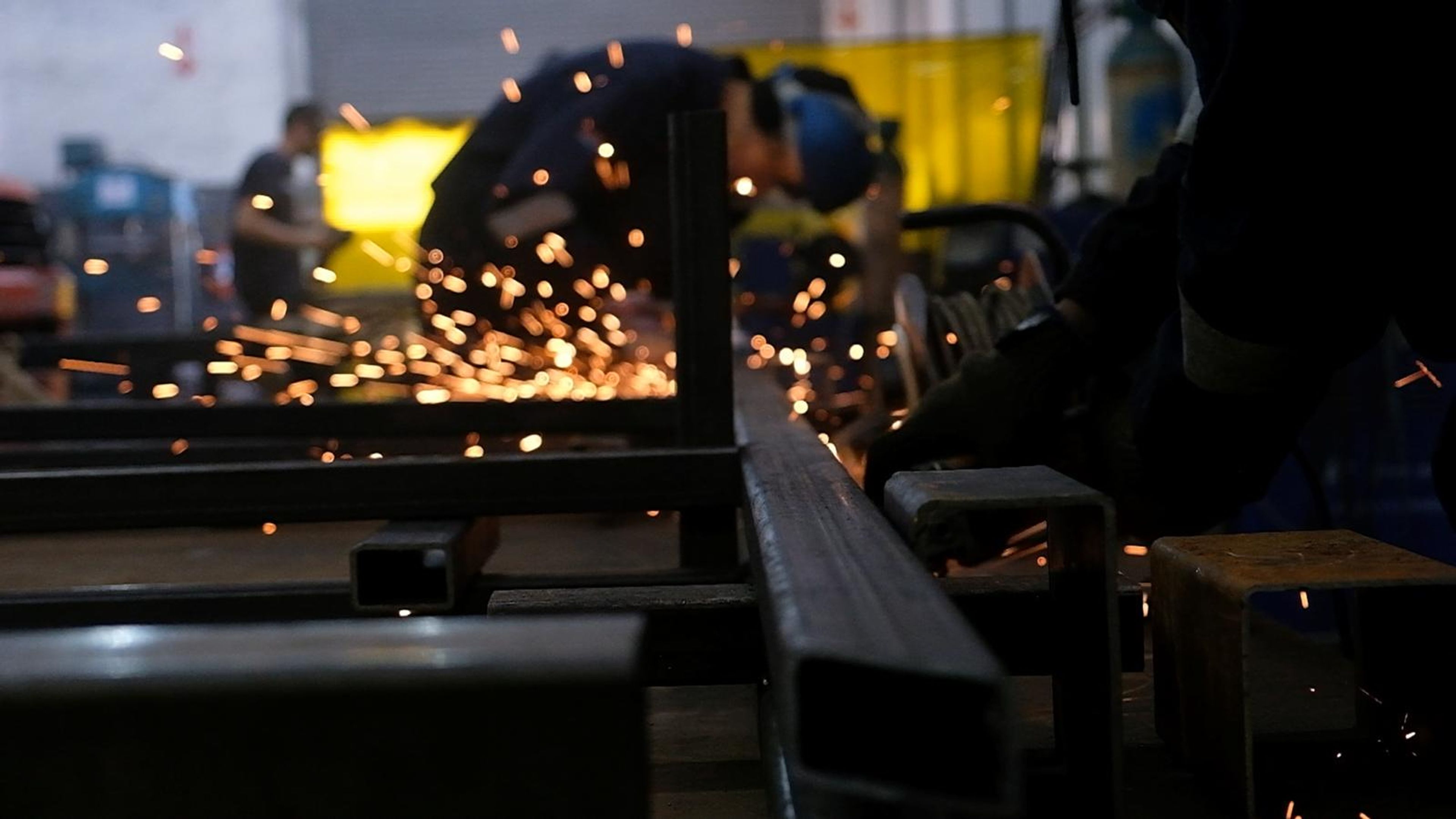 Sparks flying from grinding steel in the fabrication bay with a worker behind