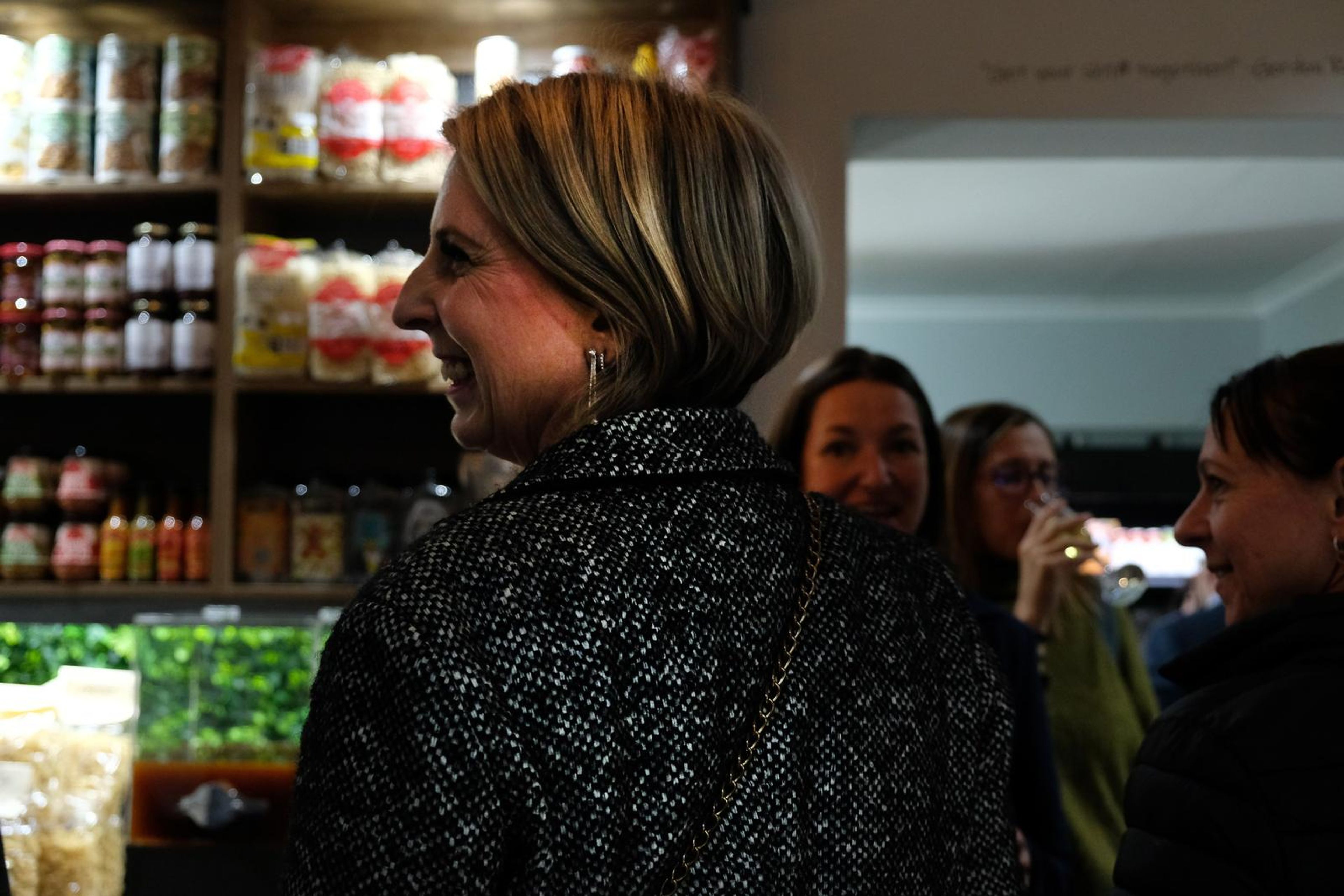 Laughing guest in a tweed jacket with other guests behind her