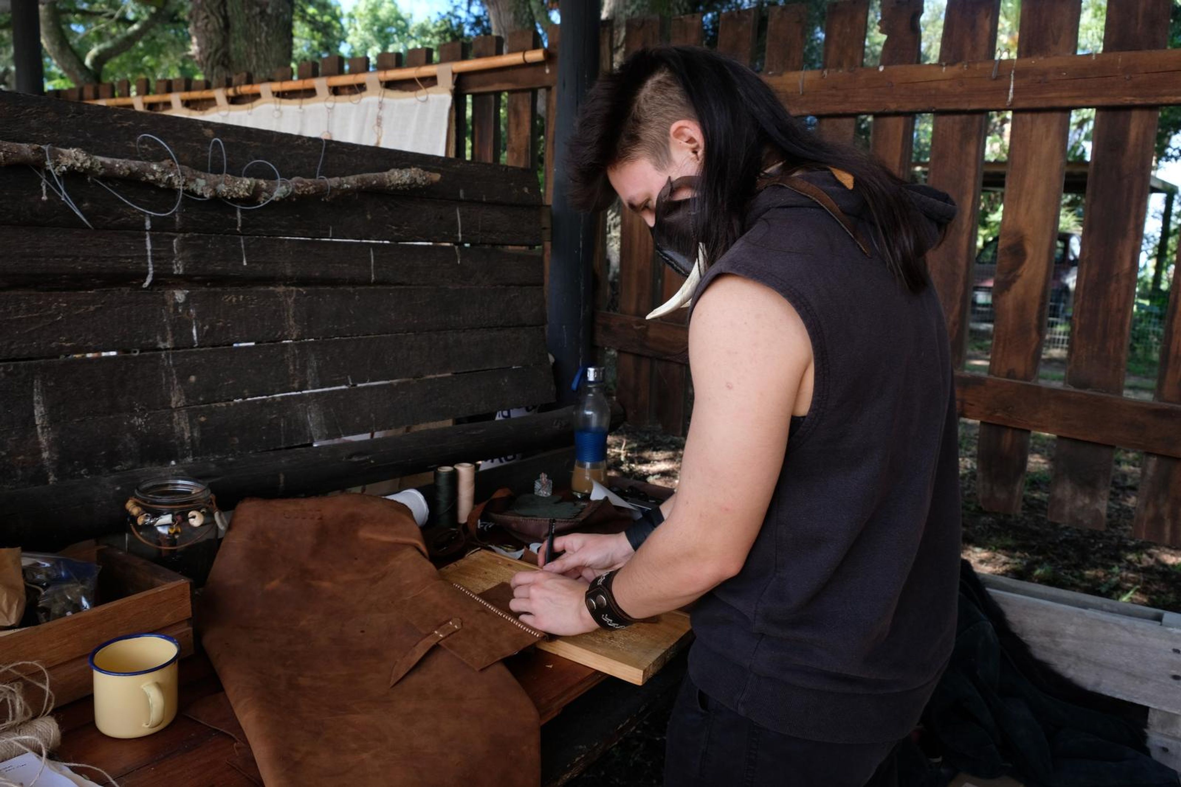 Juuks leatherworker hand-stitching at a table outdoors at the market
