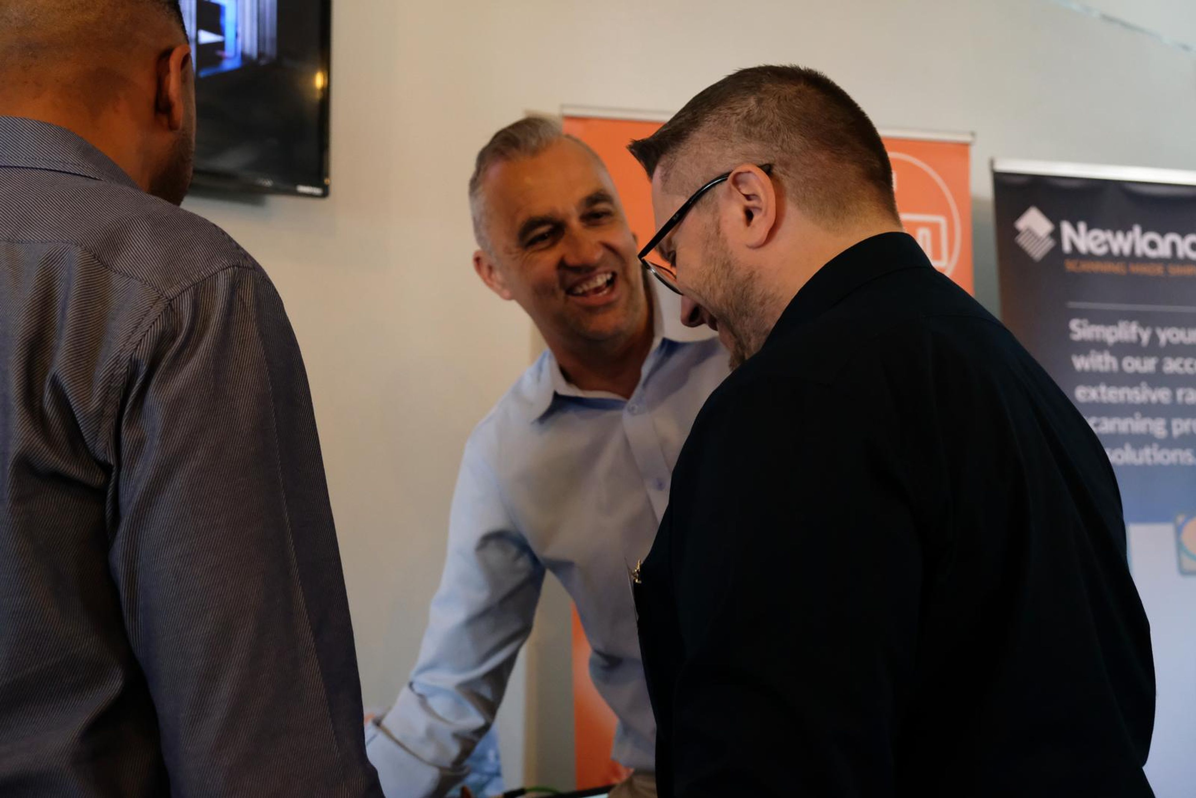 Three men sharing a laugh in front of a Newland AIDC banner