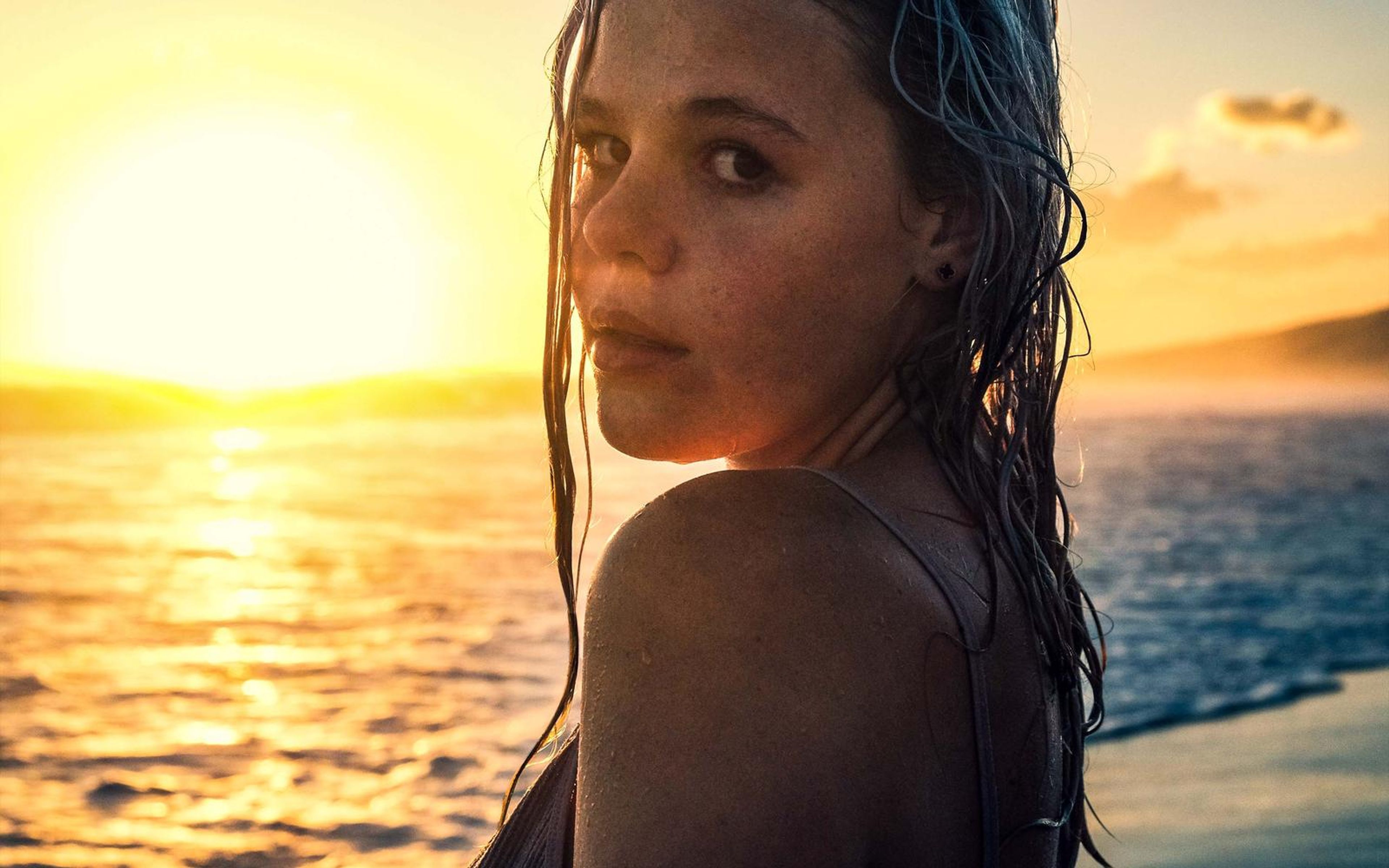 Portrait of a woman looking back over her shoulder in warm sunset light, wet hair, sea in the distance