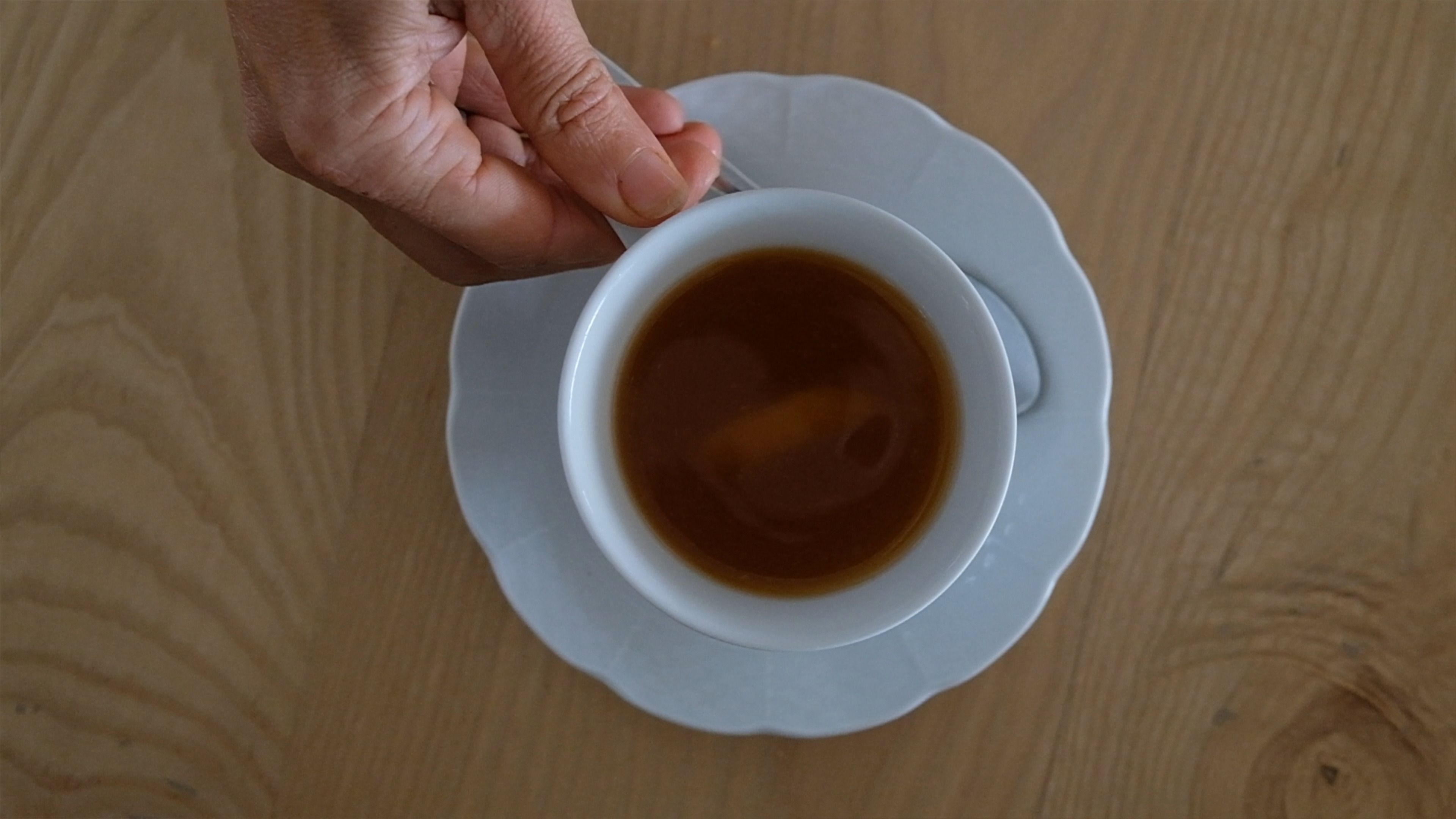 Overhead view of a hand holding a cup of tea on a saucer