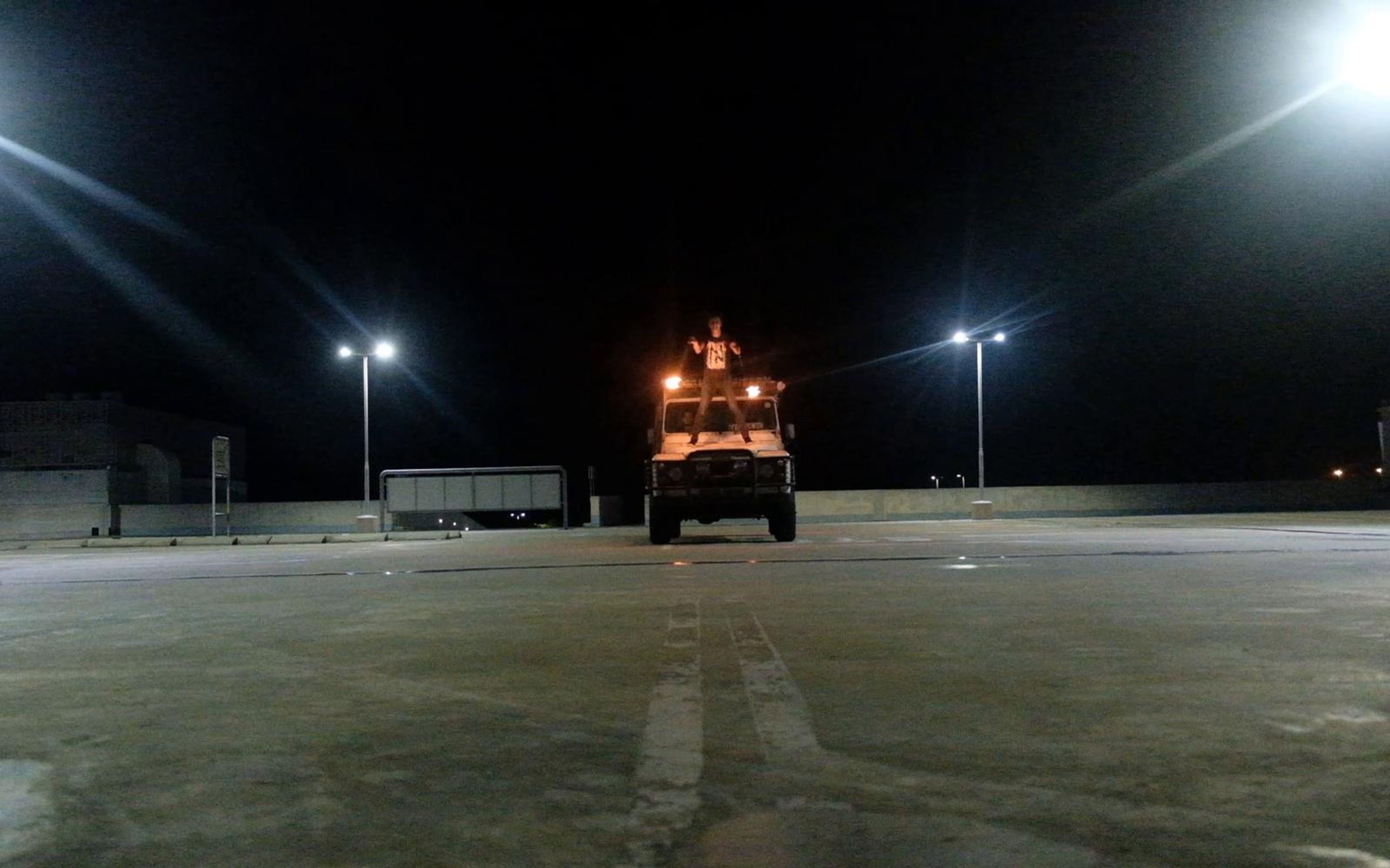 Vehicle with fire on its roof in a floodlit empty car park at night