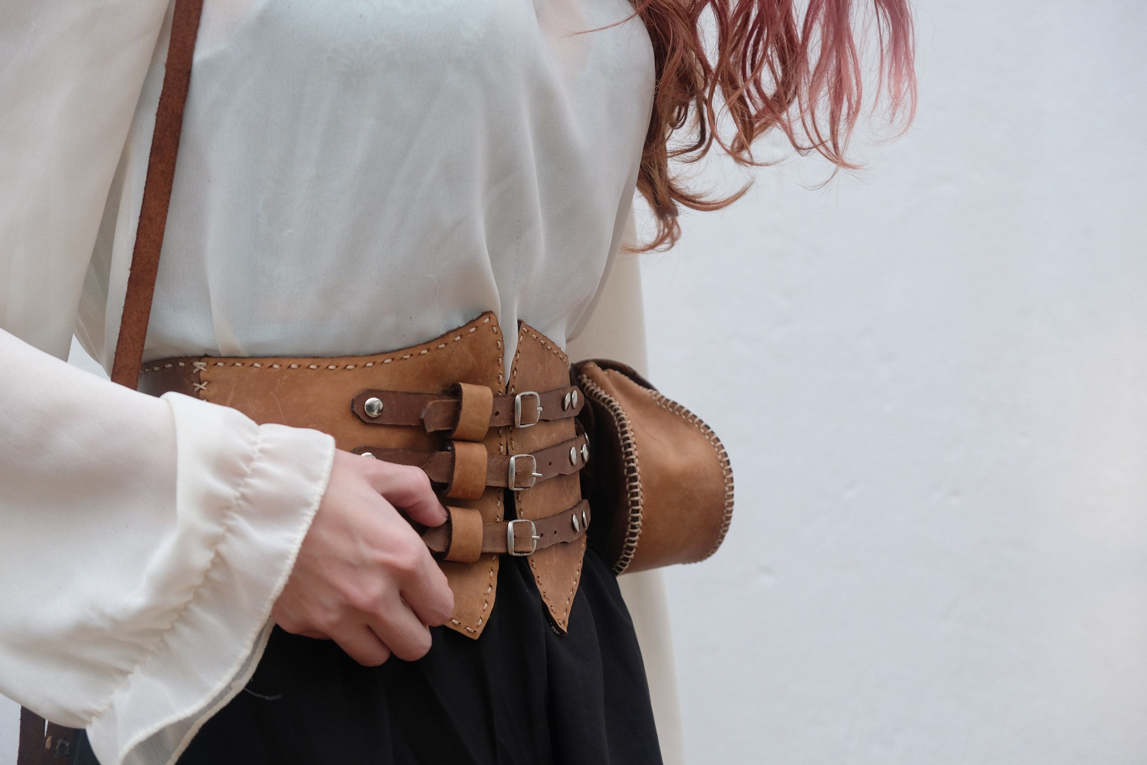 Woman touching the buckles of the tan leather corset belt