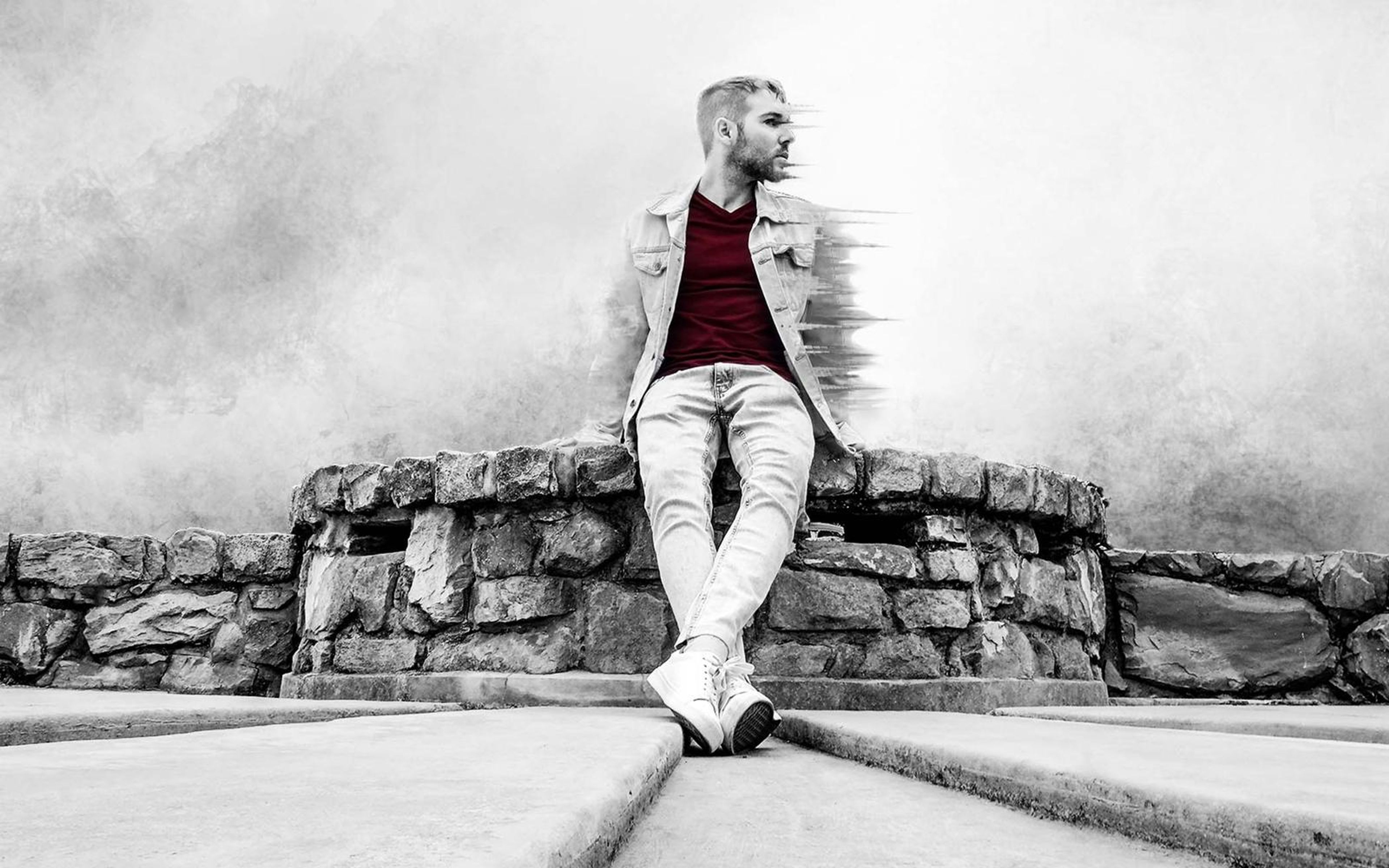 Wider framing of the seated man on the stone wall with mist rising behind and steps in the foreground