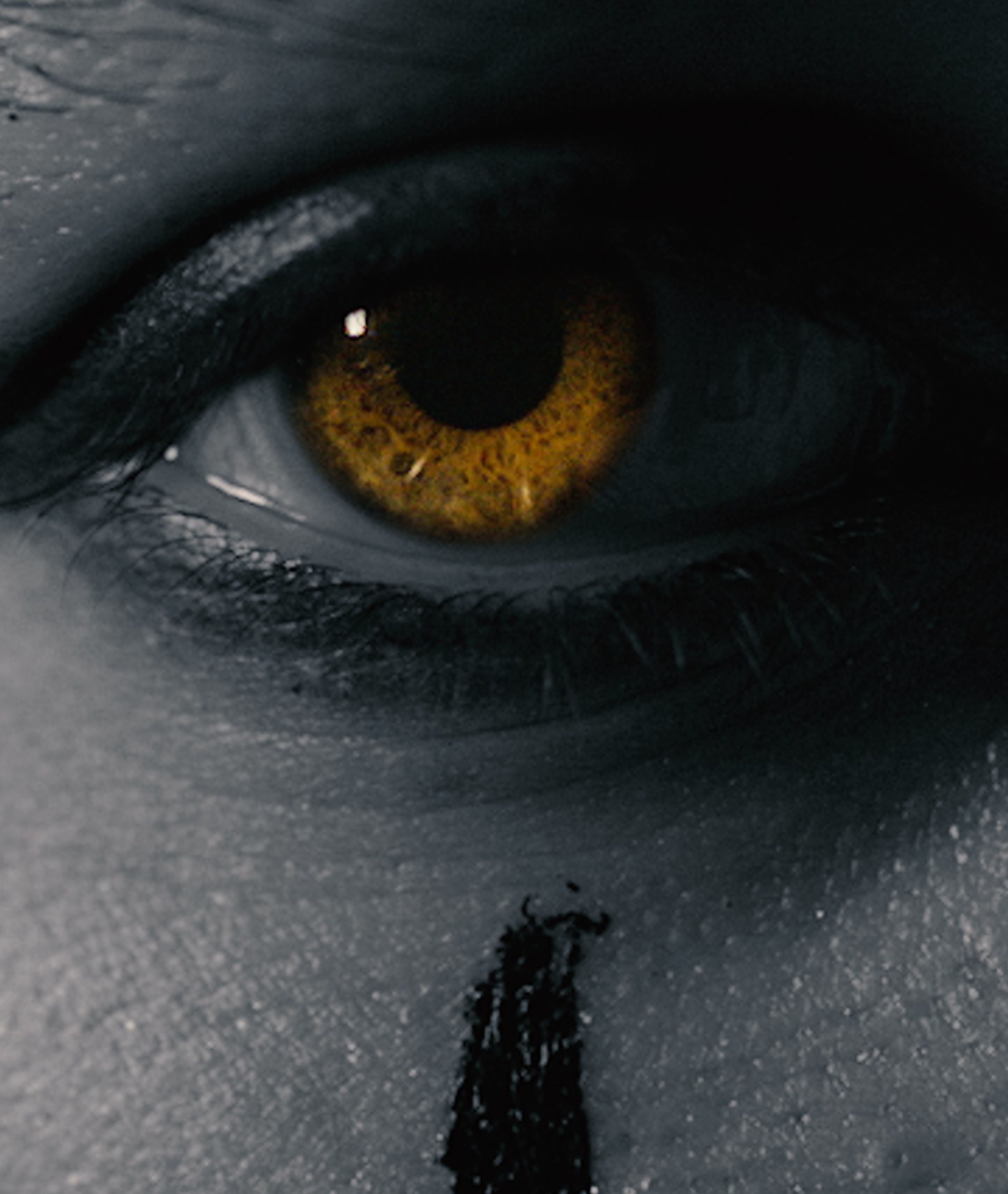 Extreme close-up of a glowing amber eye with black paint beneath it