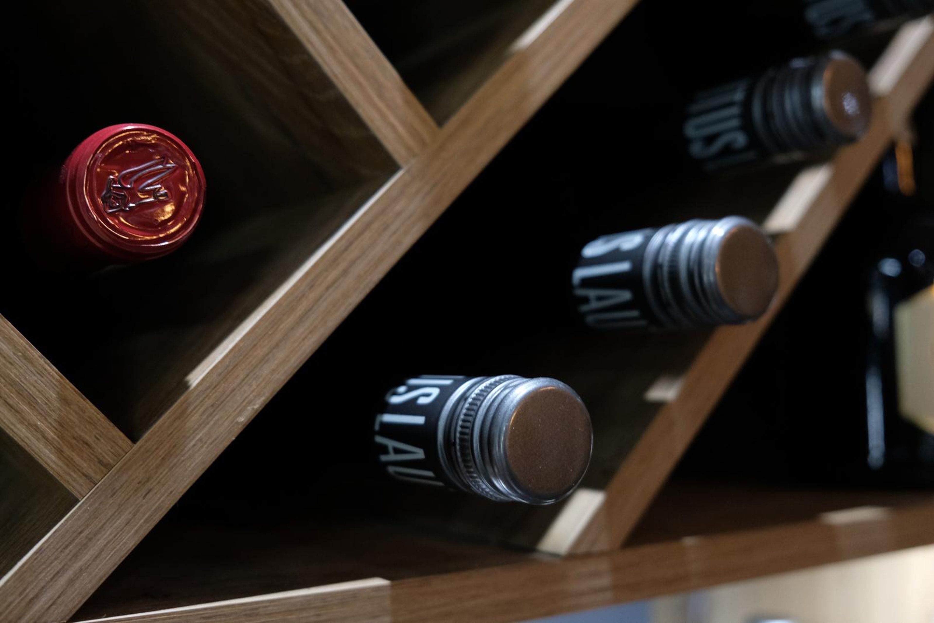 Close-up of a wine bottle with a red cap in an angled wooden rack