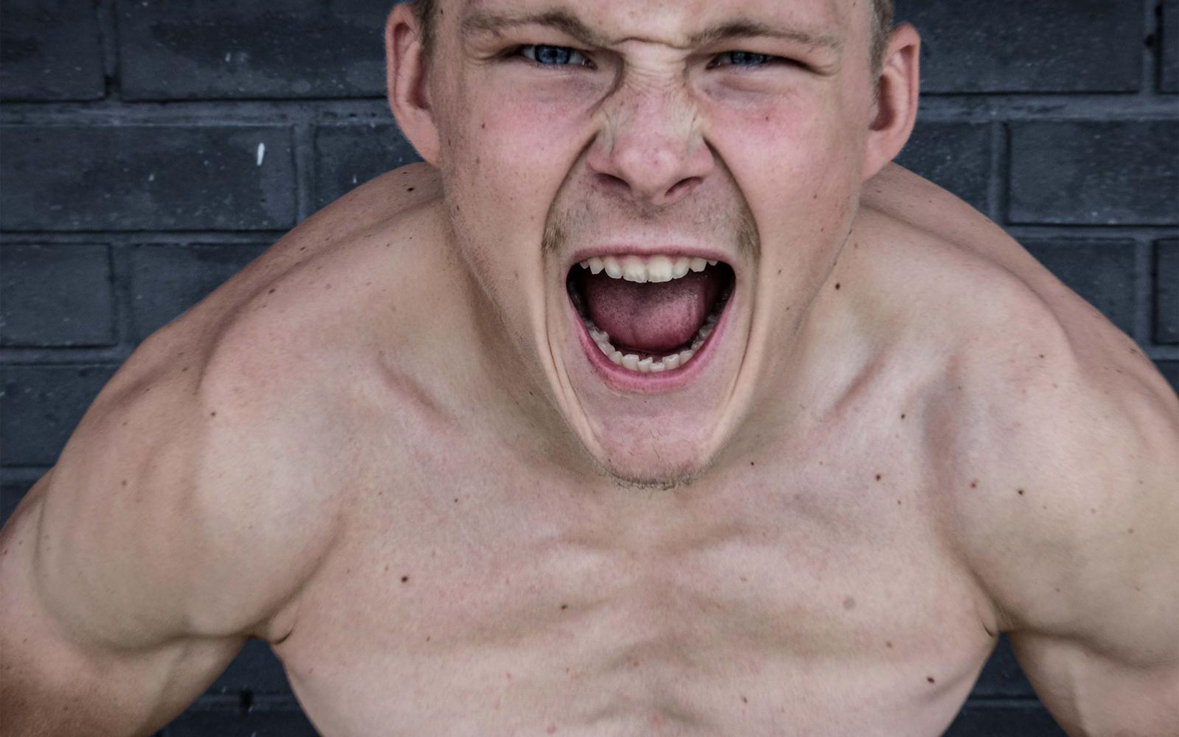 Fighter roaring toward the camera with a bare chest and flexed shoulders against dark brick