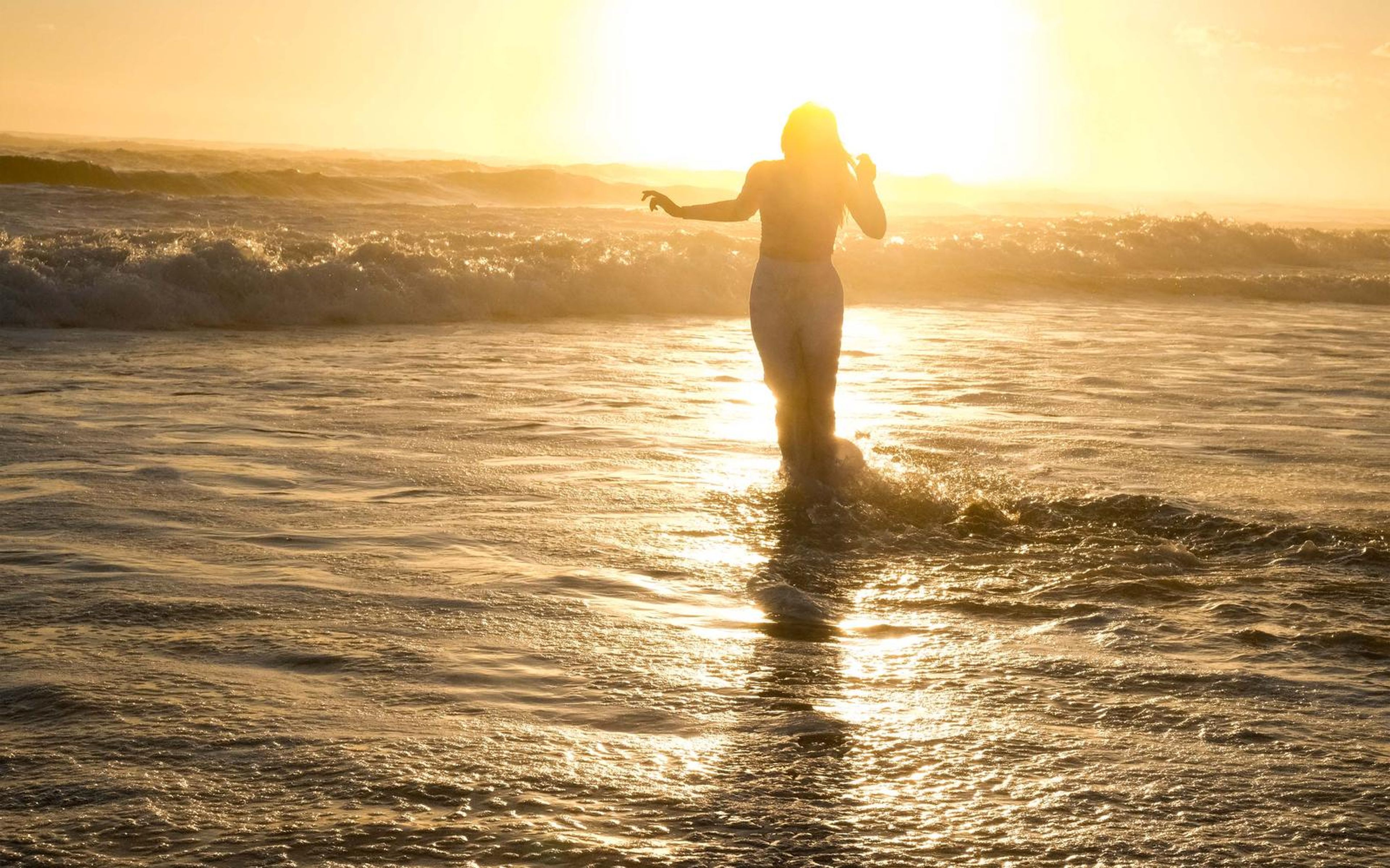 Distant woman wading into golden surf with her arms out
