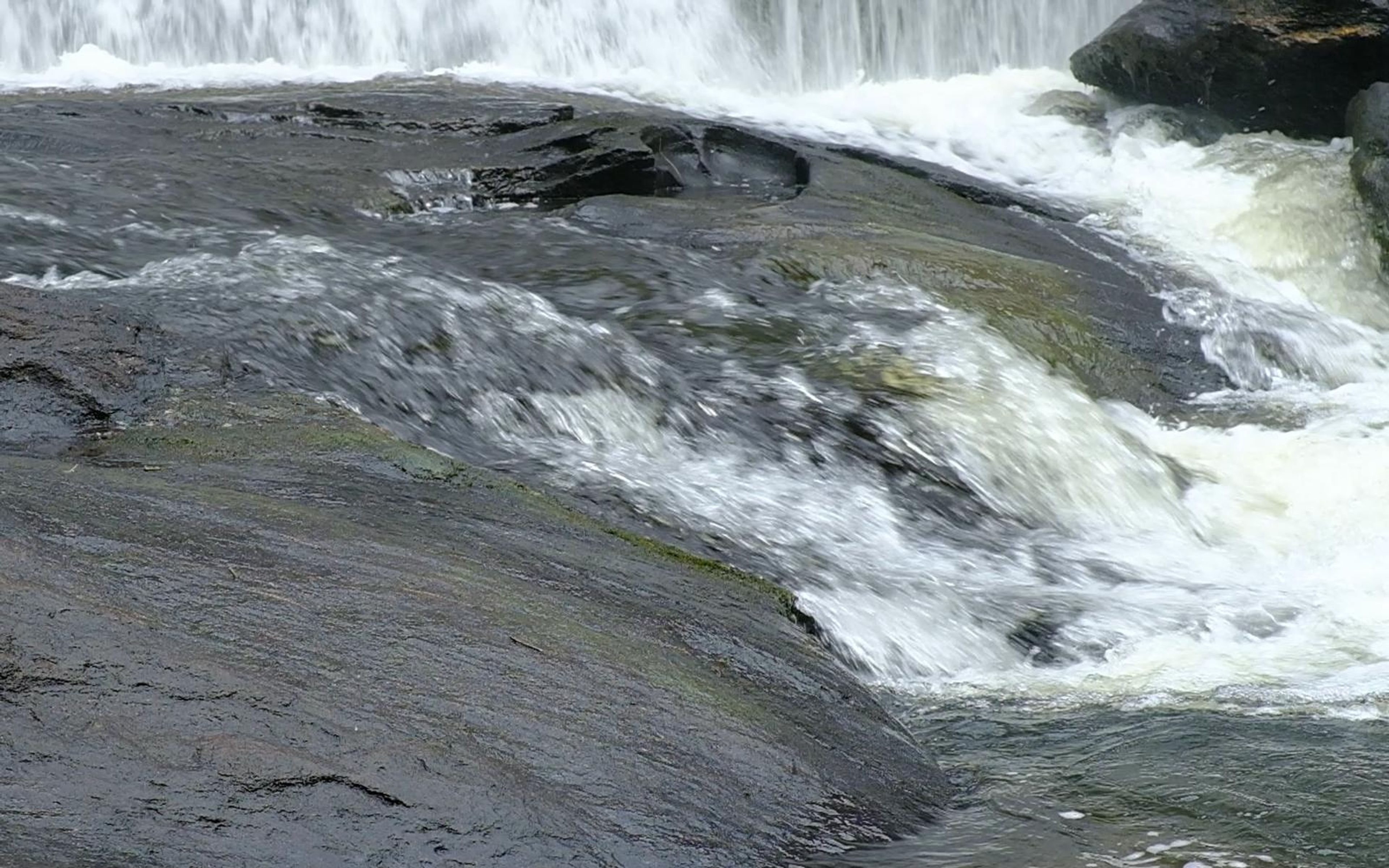 Smooth rock slab with fast water sliding over it toward the falls