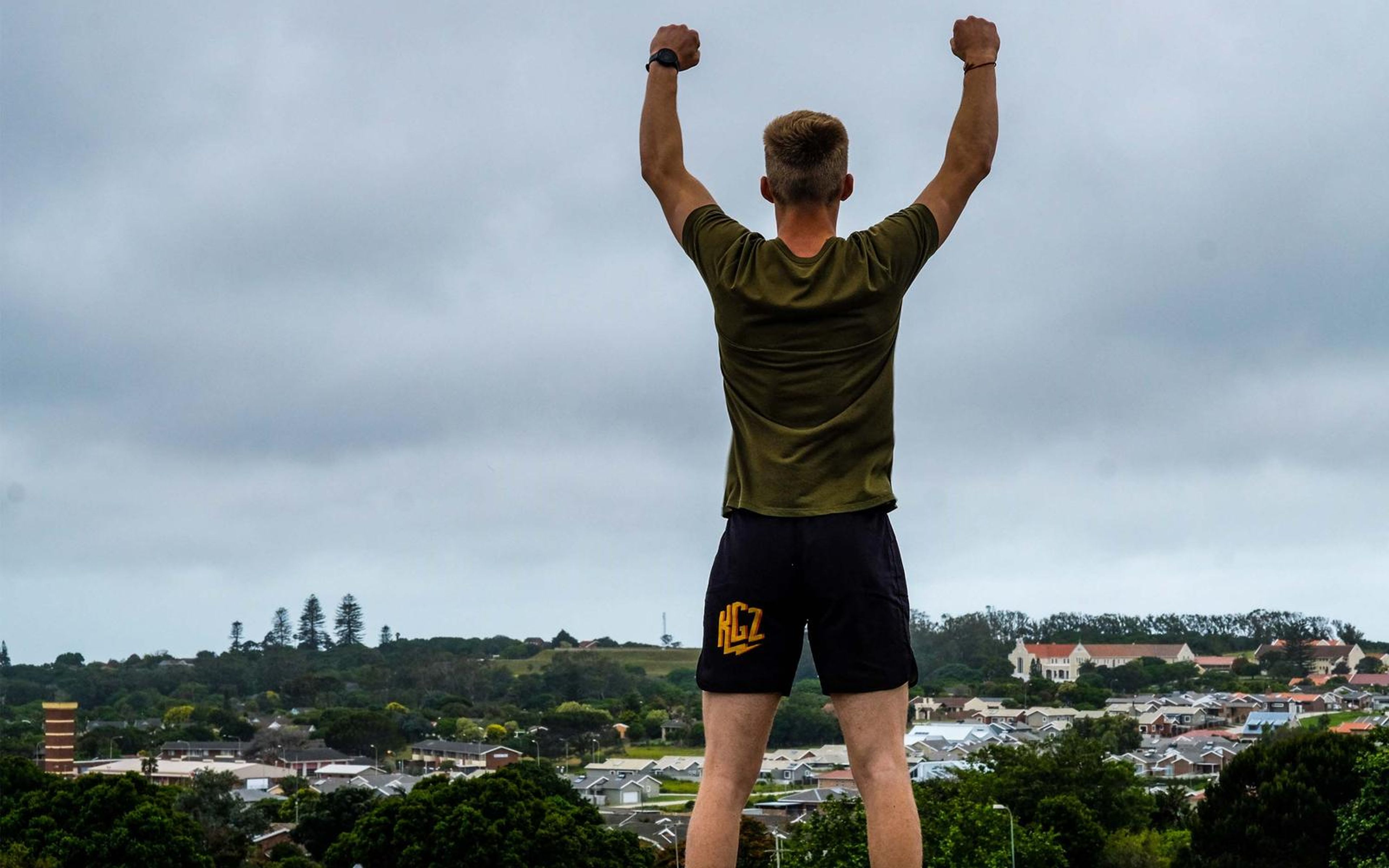 Fighter seen from behind on a hilltop with both fists raised above his head and the town spread out below