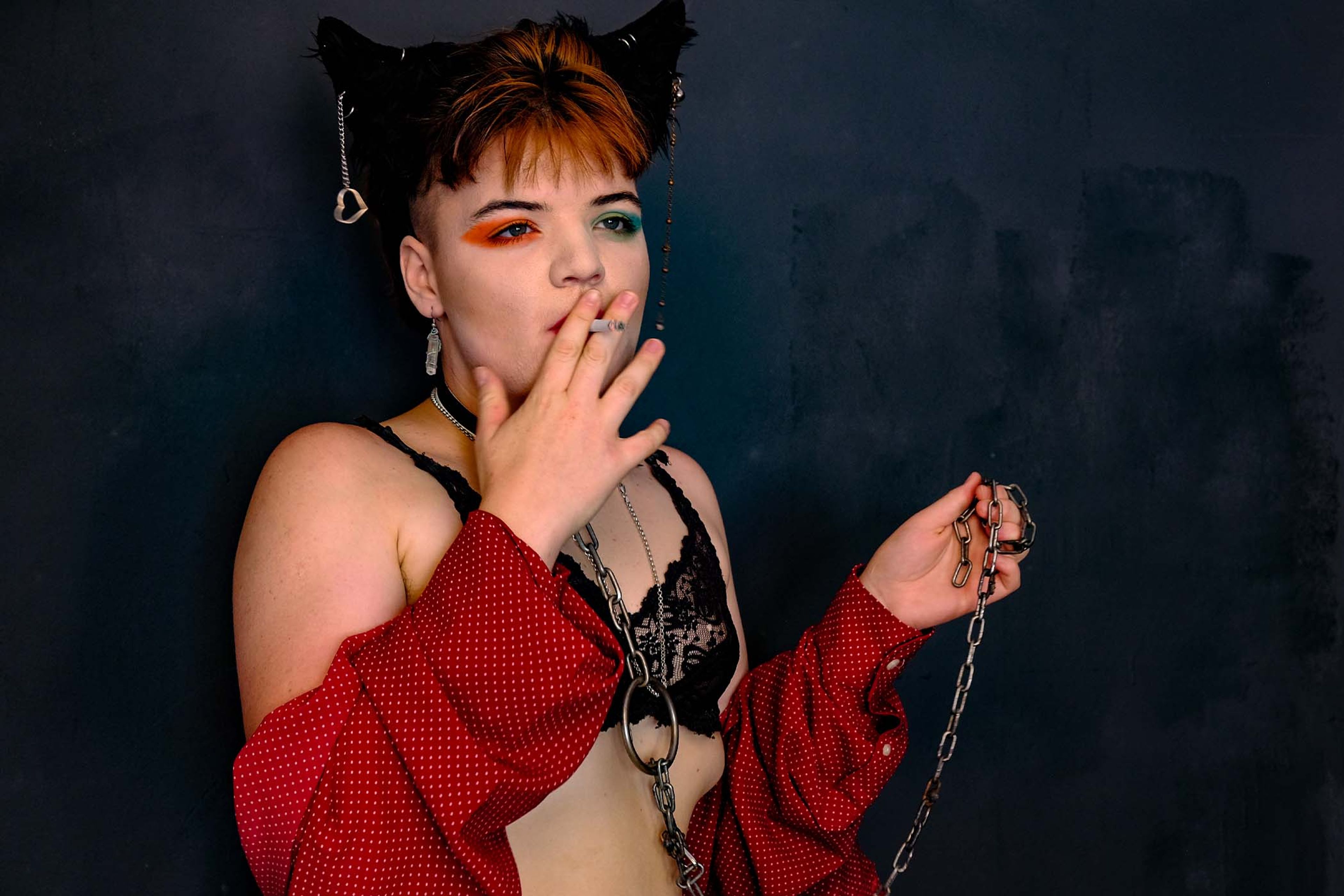 Portrait, subject in a lace bra and cat-ear headpiece smoking a cigarette, holding a chain