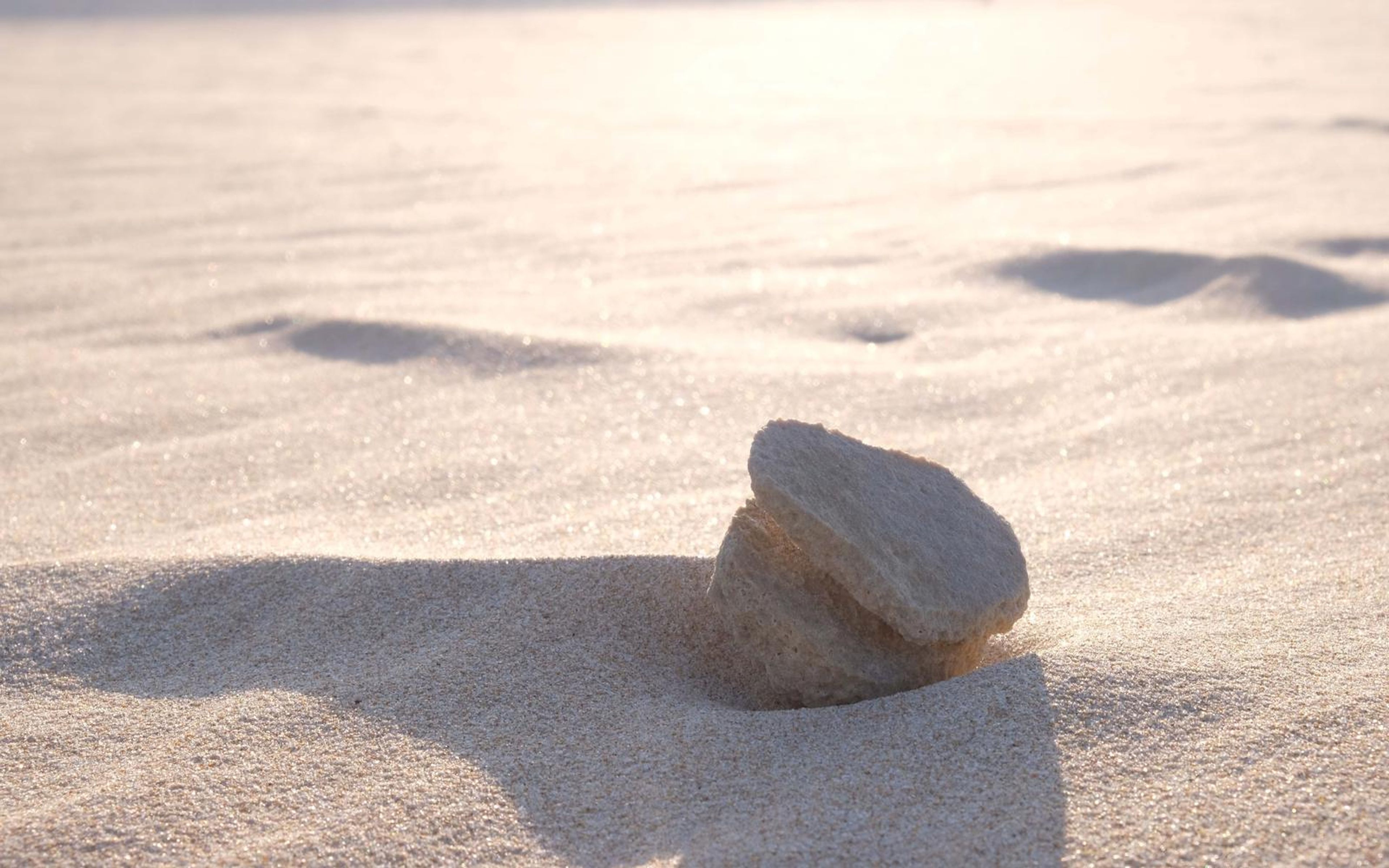 Small rock casting a long shadow on bright sand in low light