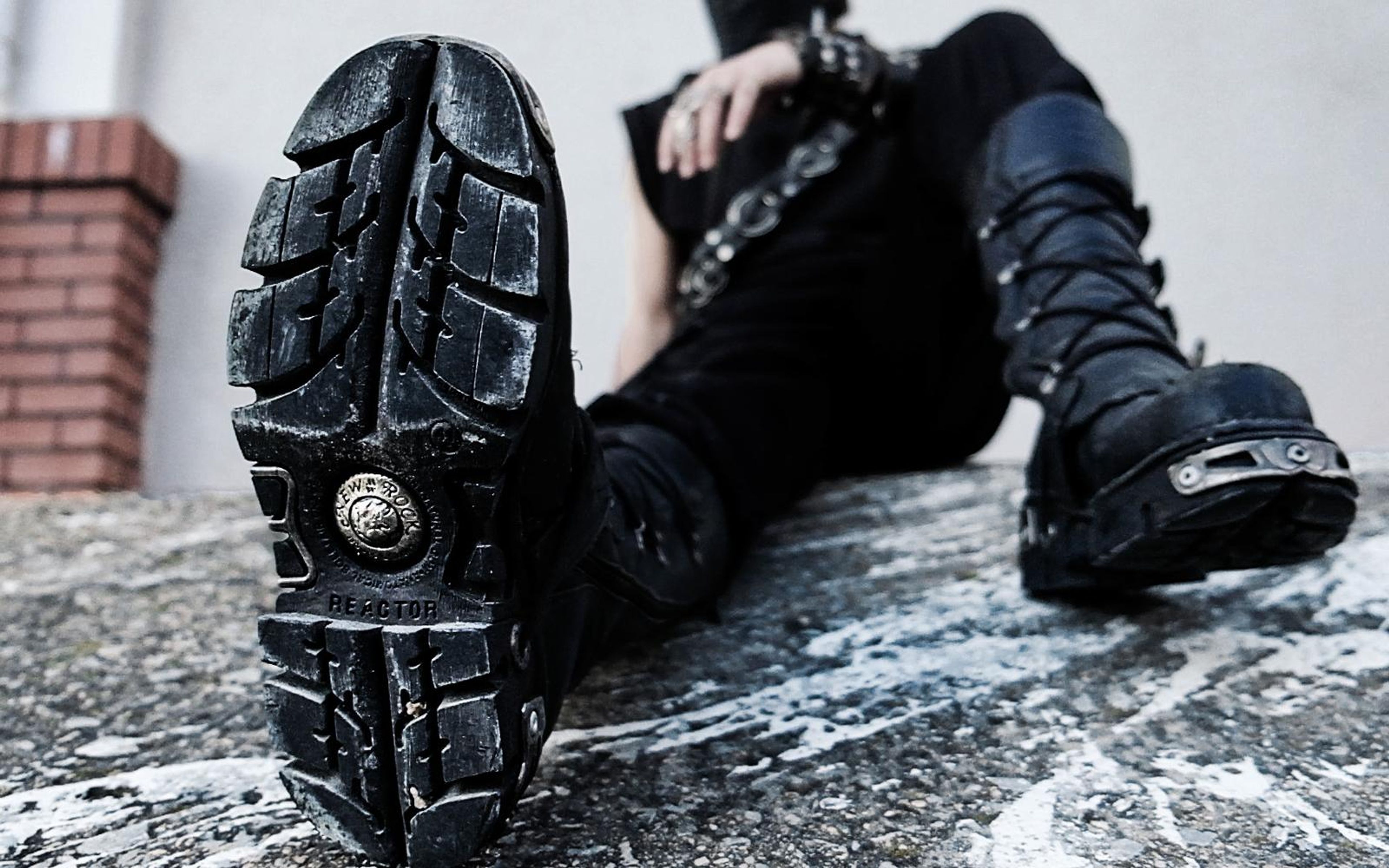 Low angle view of a boot sole with a round emblem as the performer reclines on a concrete ledge with brick behind