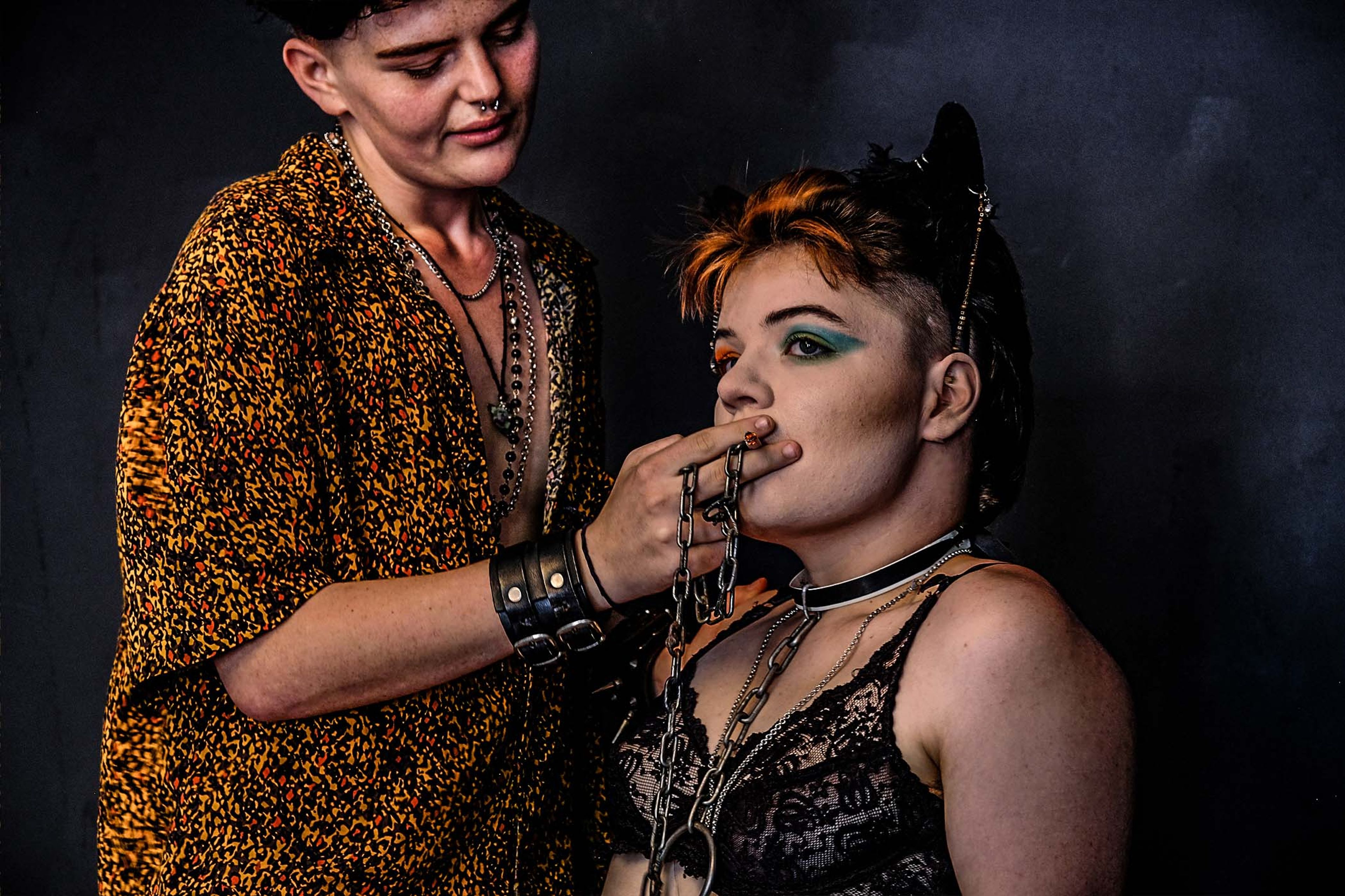 Portrait of a couple, one feeding the other a chain link, both in patterned and lace tops