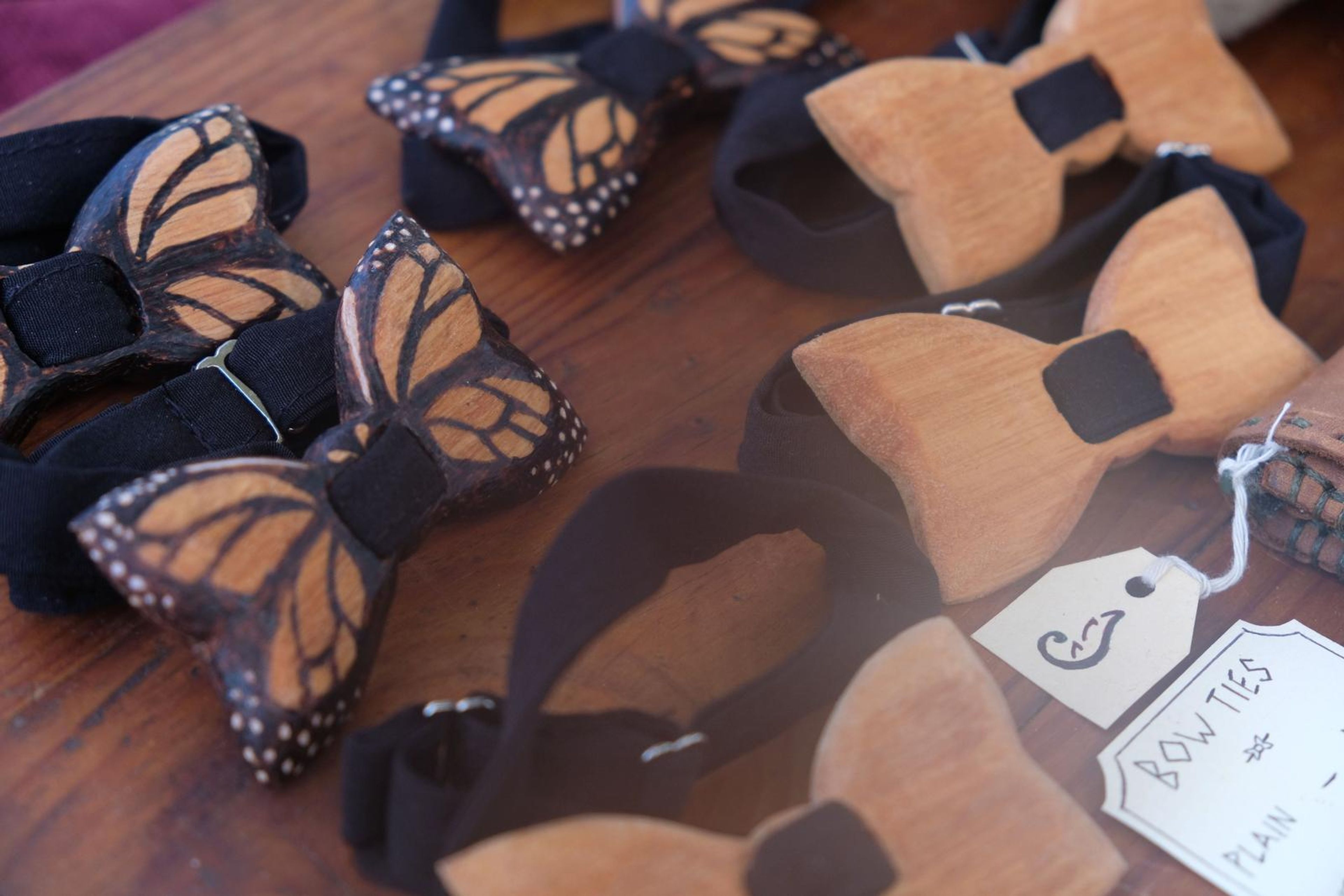 Carved wooden bow ties, including butterfly designs, beside a leather pouch