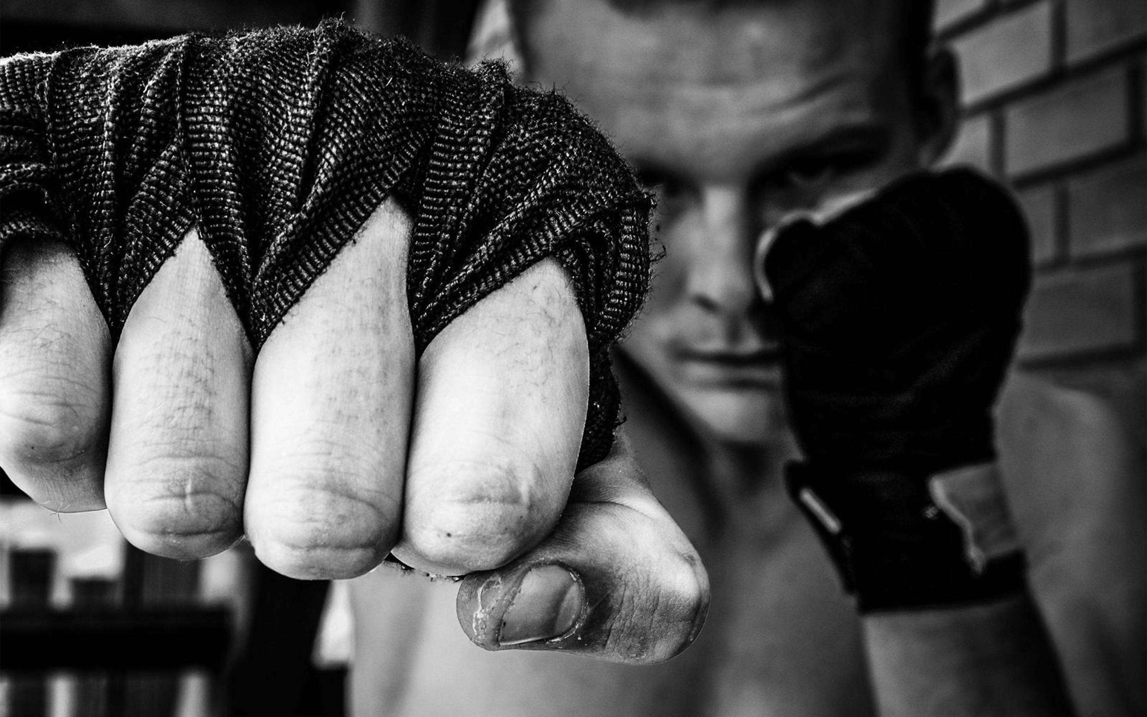 Black and white close shot of a wrapped fist pushed toward camera with the man's face blurred behind