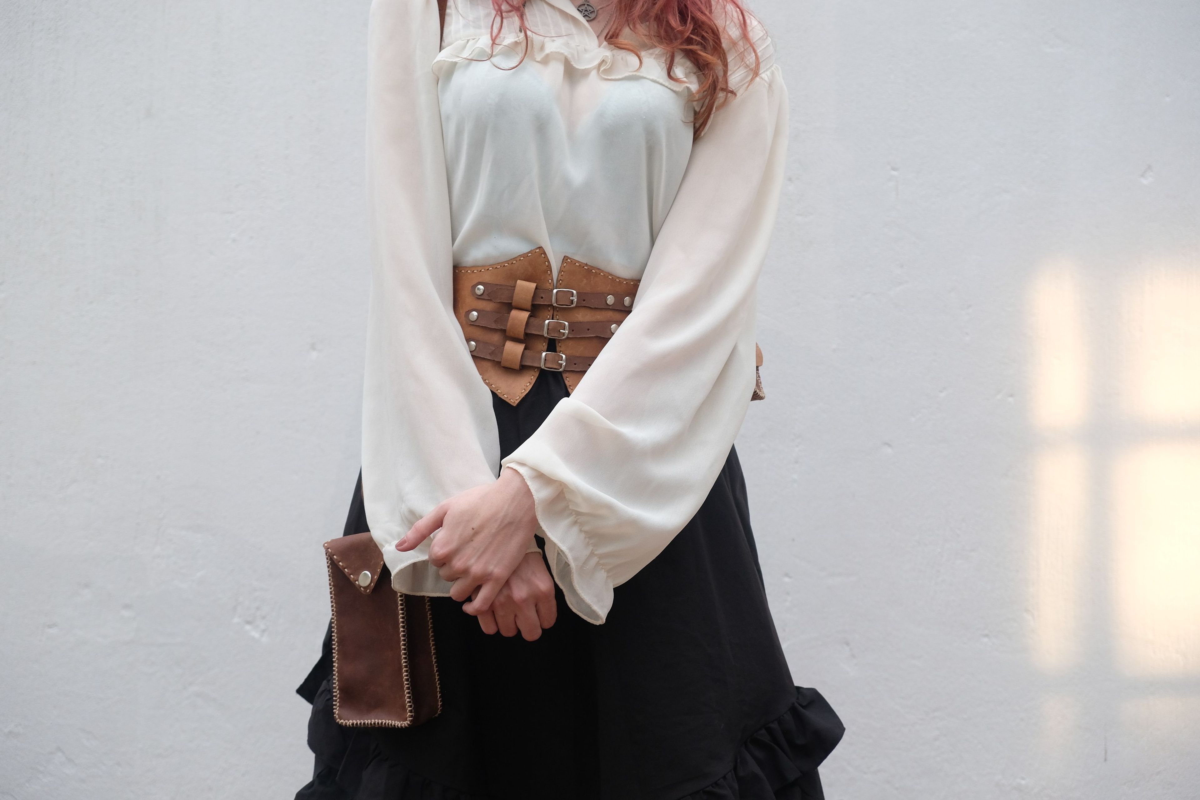 Woman standing with her hands clasped, a leather corset belt and a brown phone bag