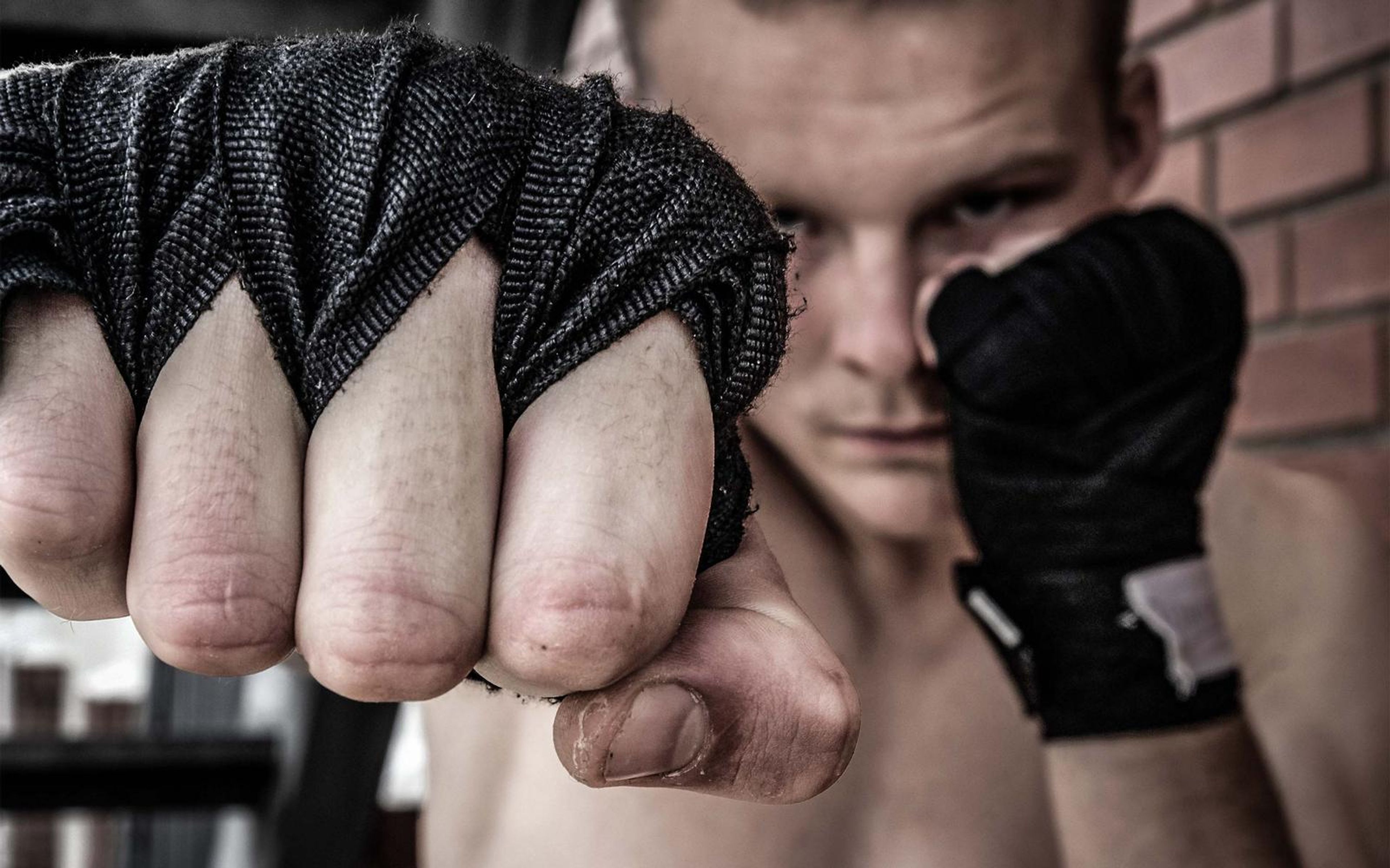 Wrapped fist pushed toward the lens with the fighter's eyes just above it, warm brick behind