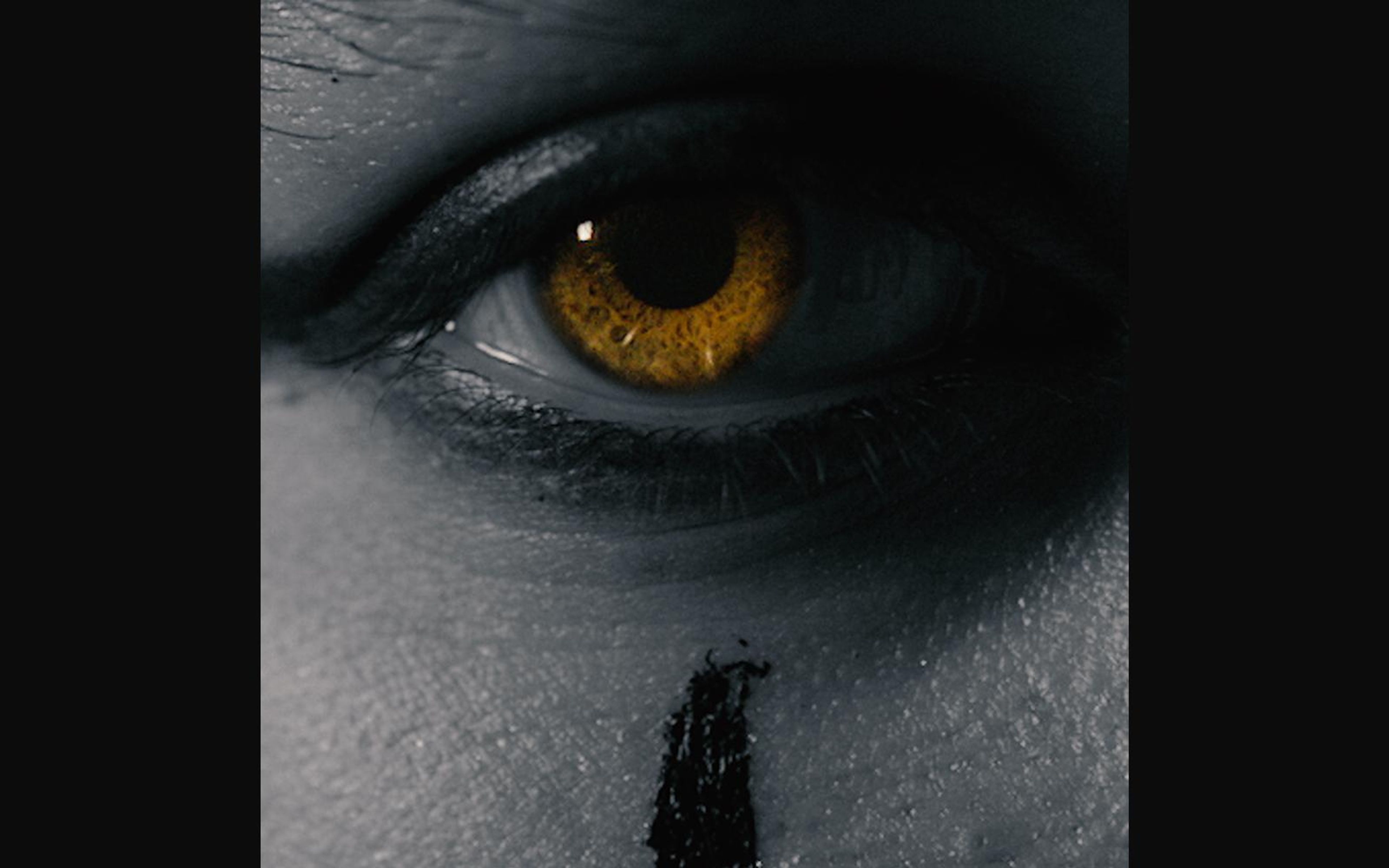 Extreme close-up of a glowing amber eye with a black paint mark below it, graded in cold grey-blue
