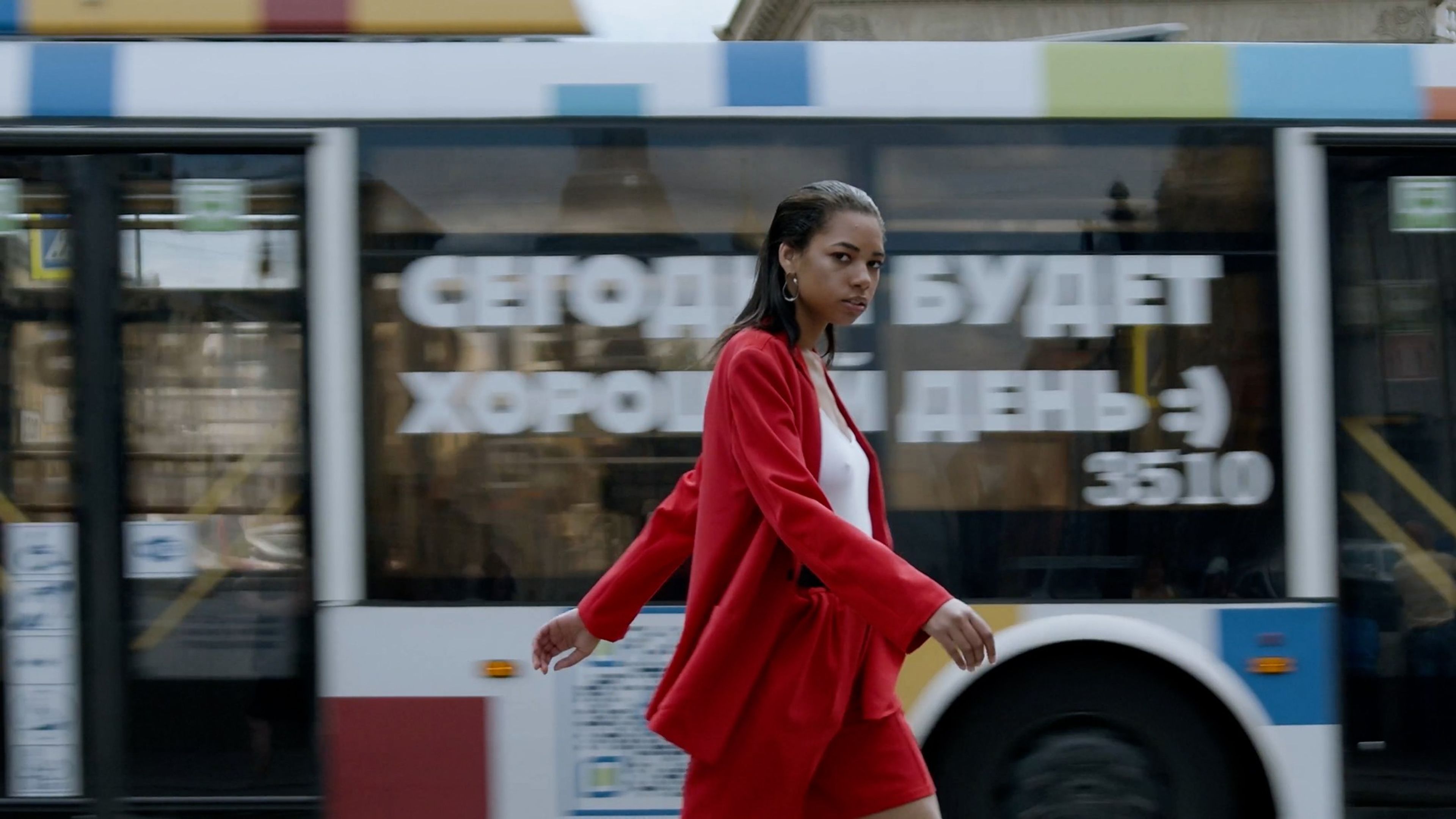 Woman in a red suit walking in front of a passing bus