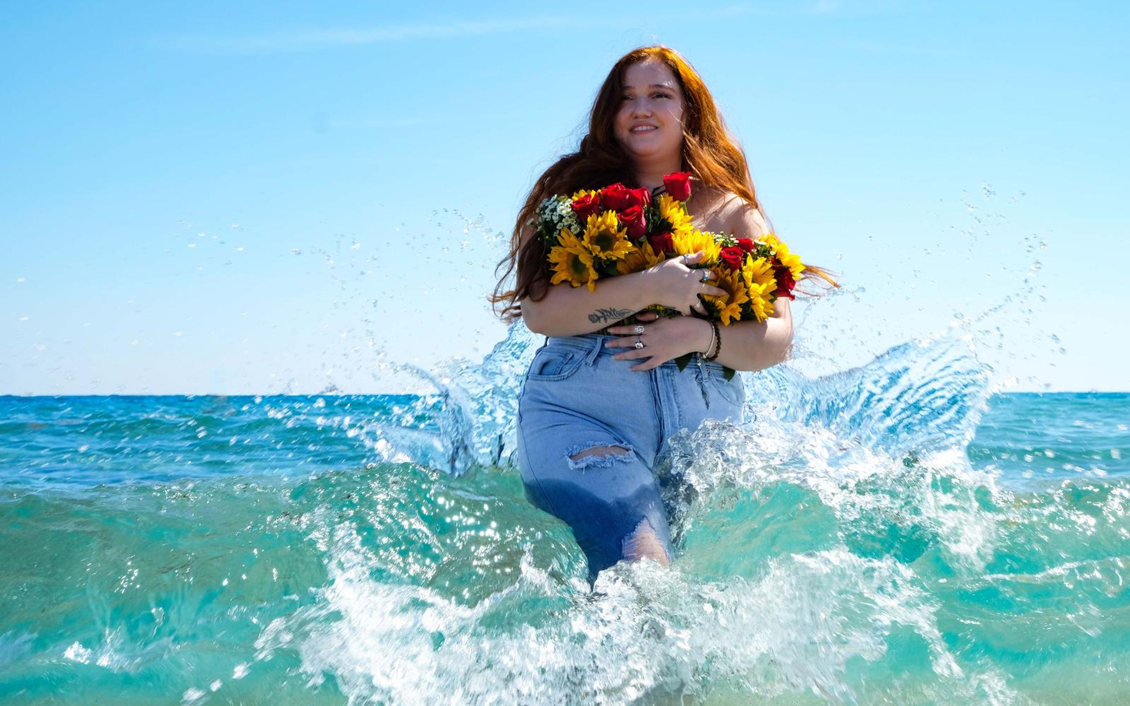 Model laughing as spray flies around her, flowers held tight, turquoise water and pale sky