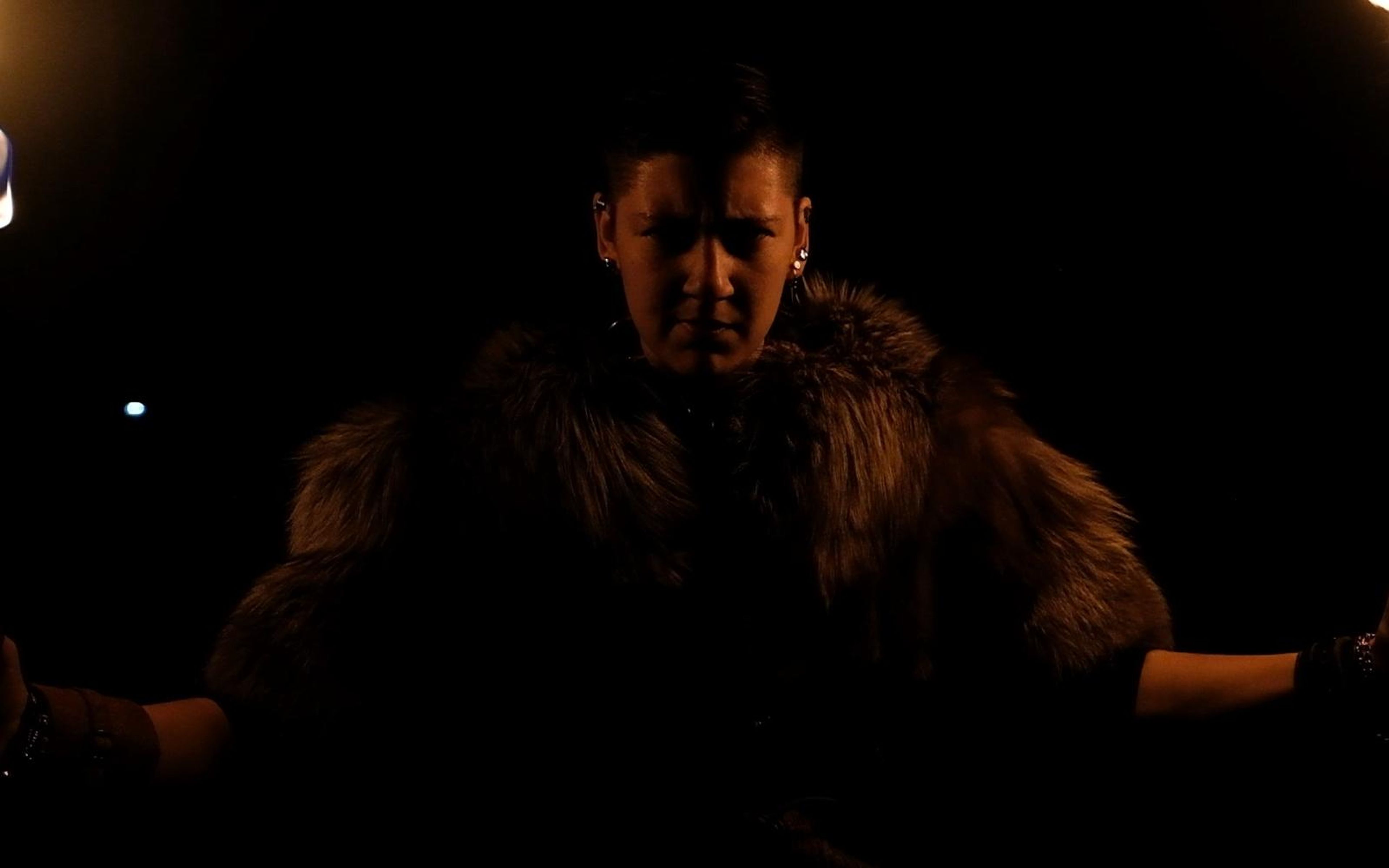 Fur-clad barbarian with arms spread, a bright torch flame in the upper corners, stern look
