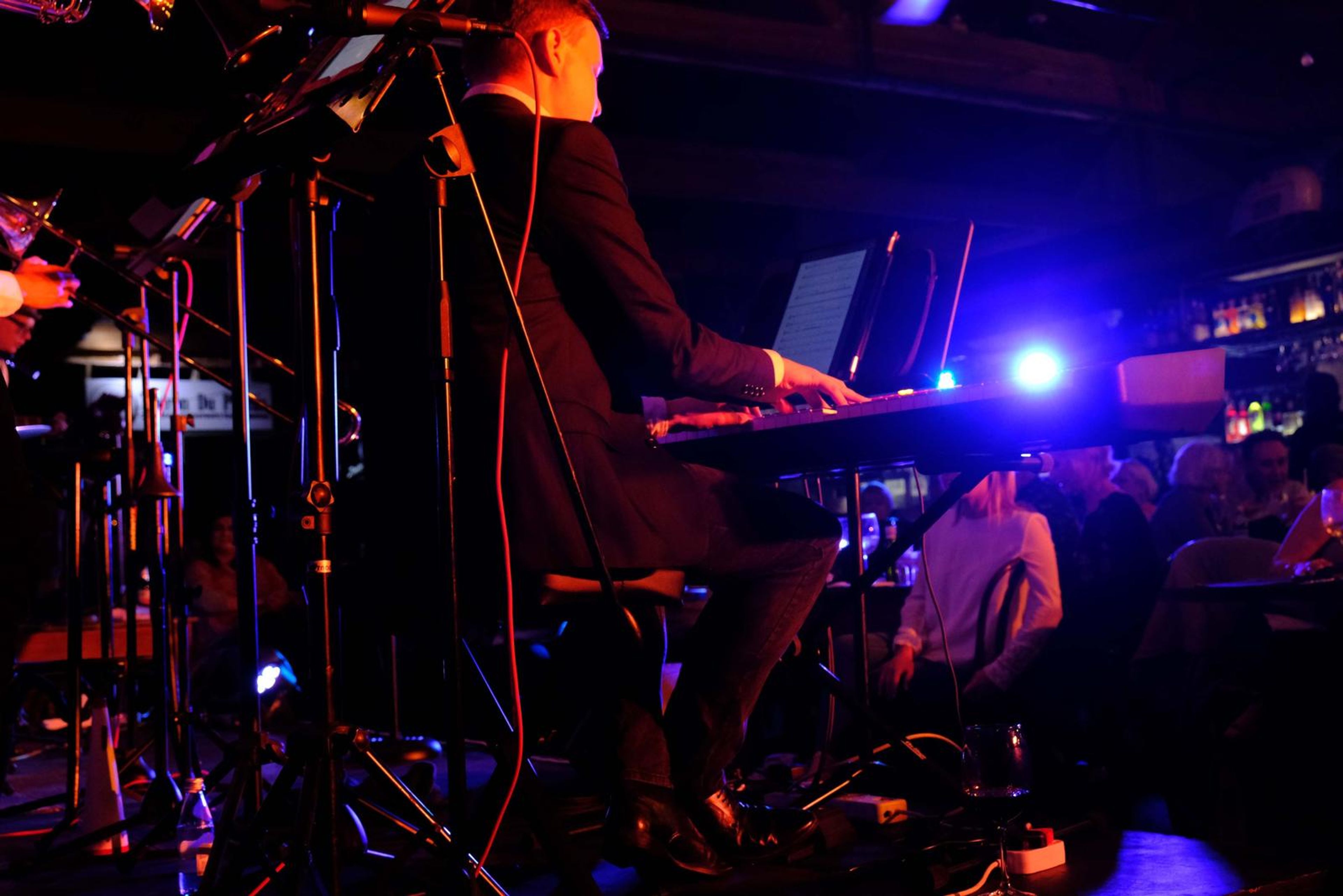 Keyboard player in a suit and the band behind a tangle of microphone stands