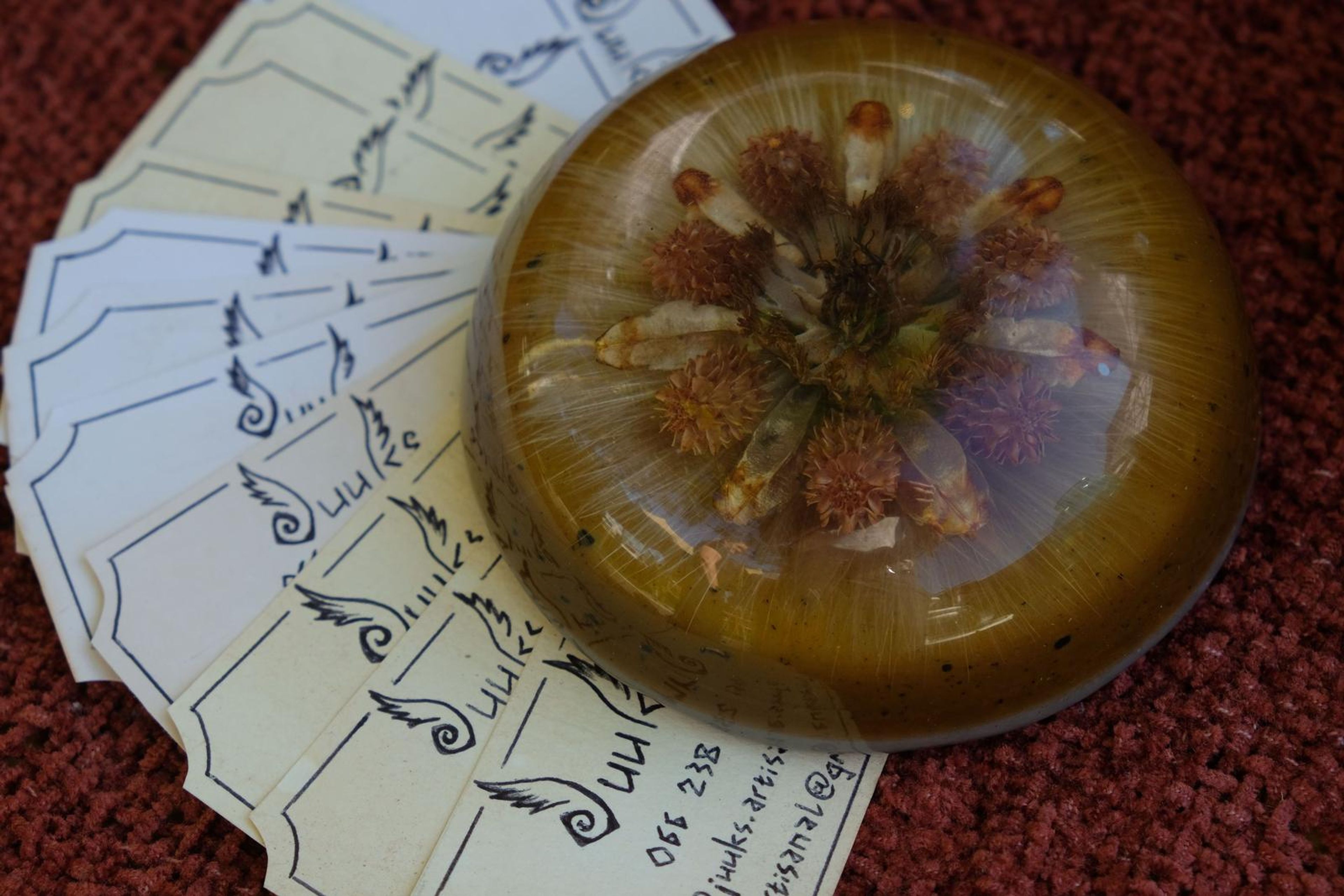 Resin dome with a dried flower beside a fan of handwritten cards