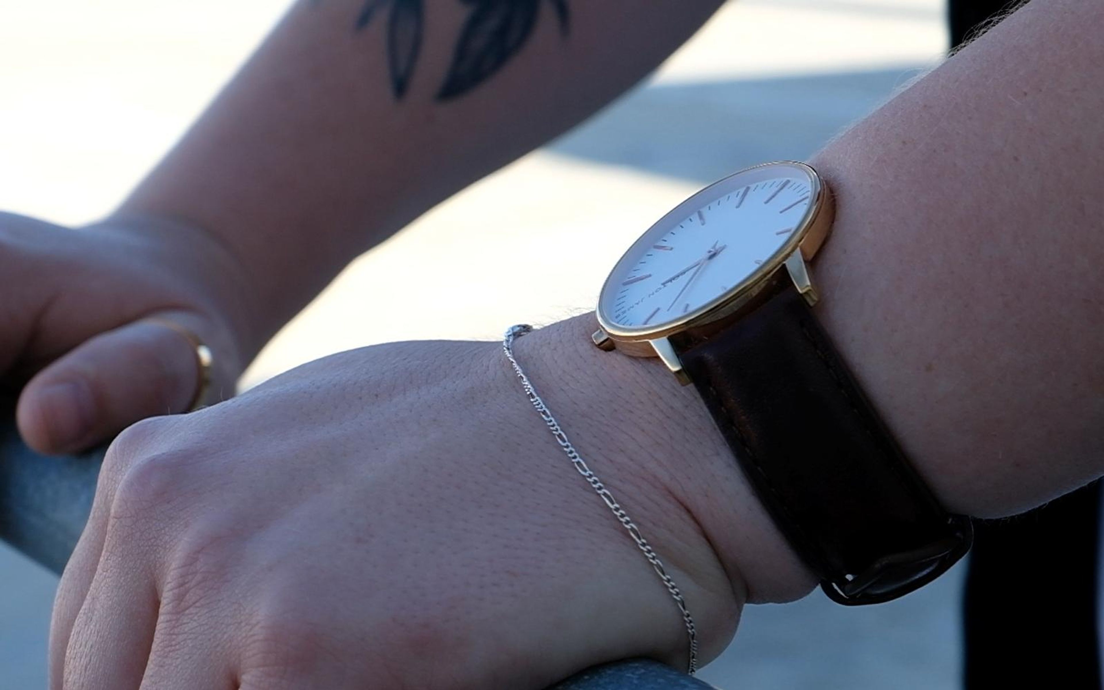Hand resting on a rail with watch and bracelet, sunlit concrete behind, shallow depth of field