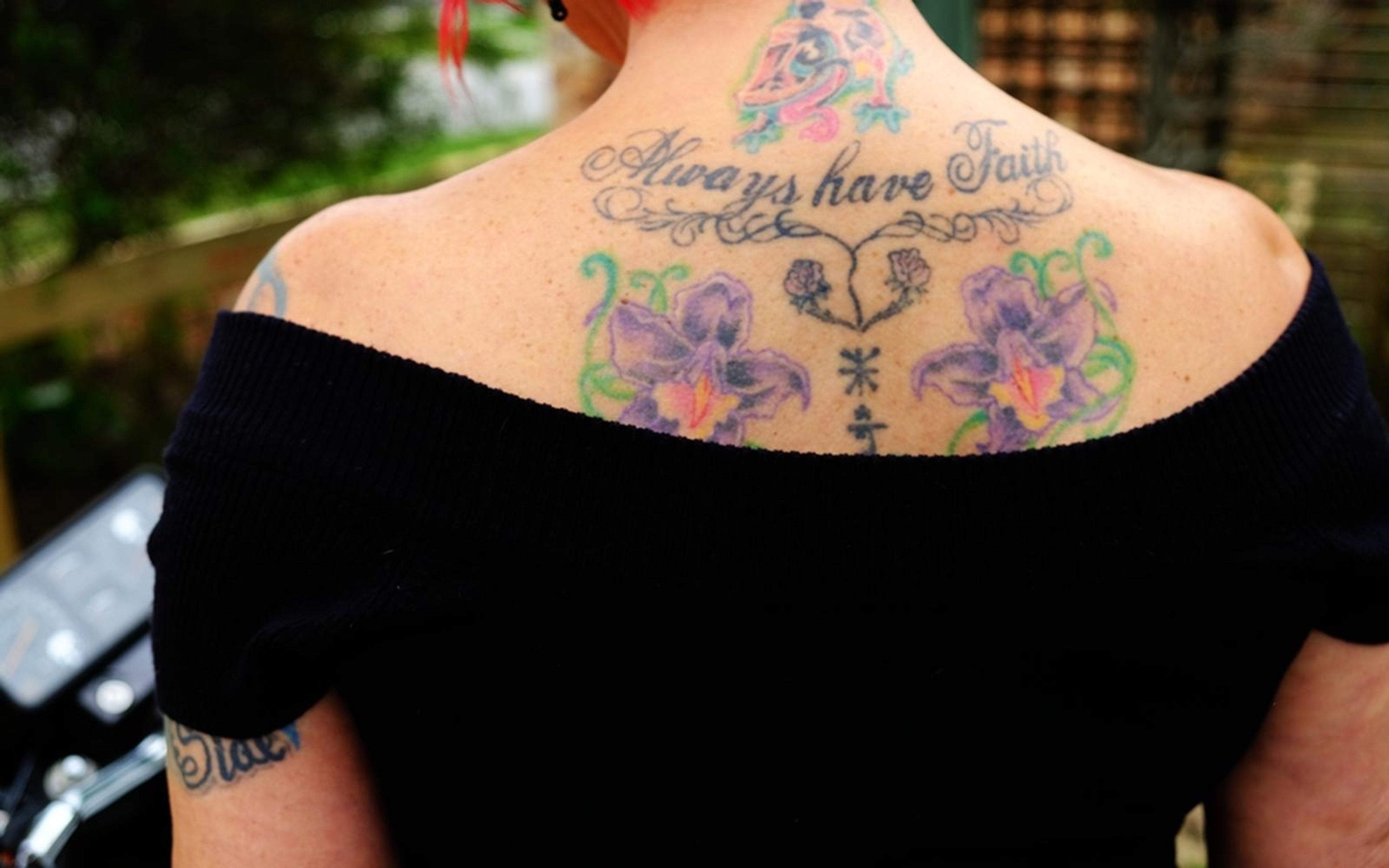 Back view of a woman in a black off-shoulder top showing a floral tattoo with script lettering