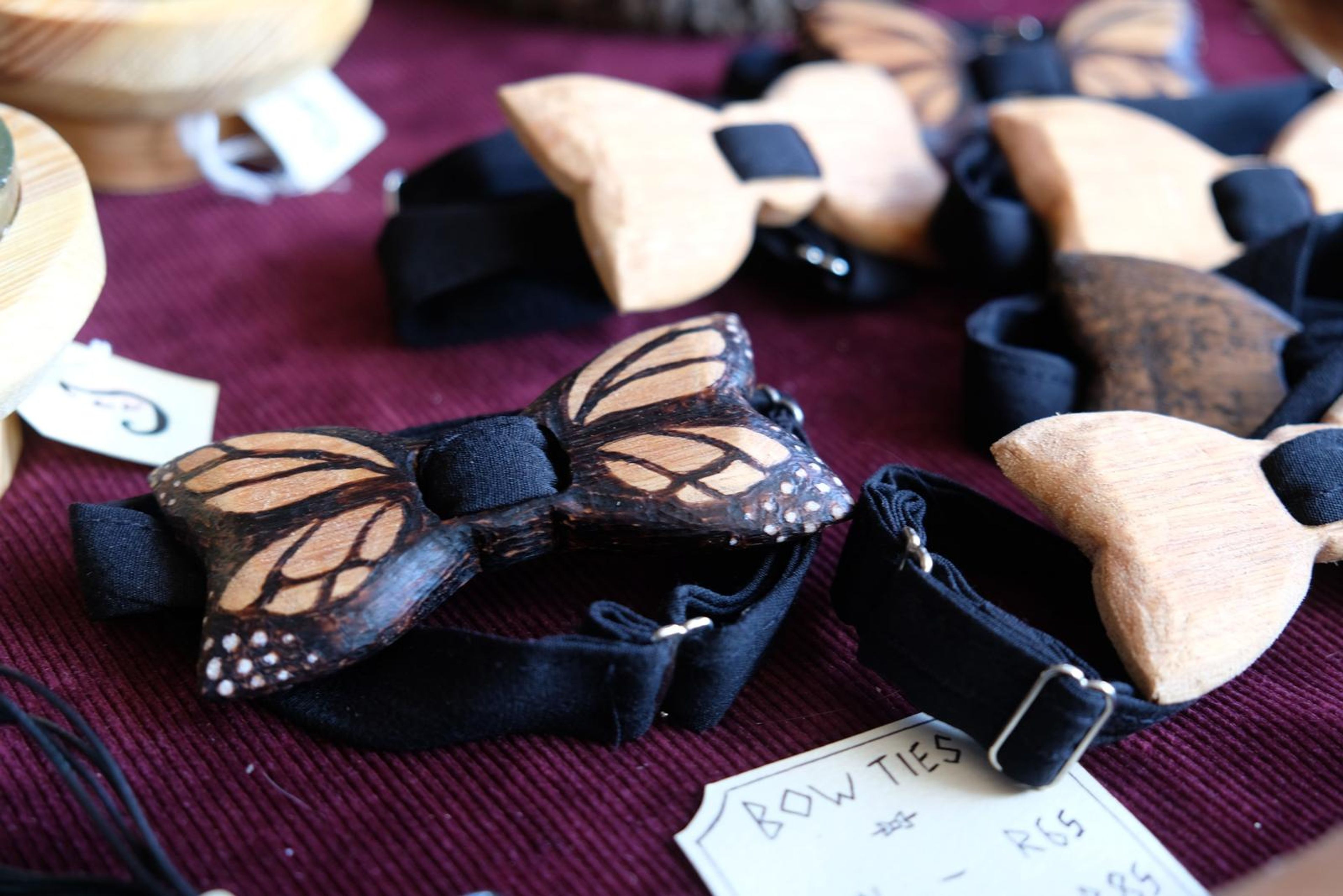 Carved wooden butterfly bow ties on elastic bands on a maroon cloth