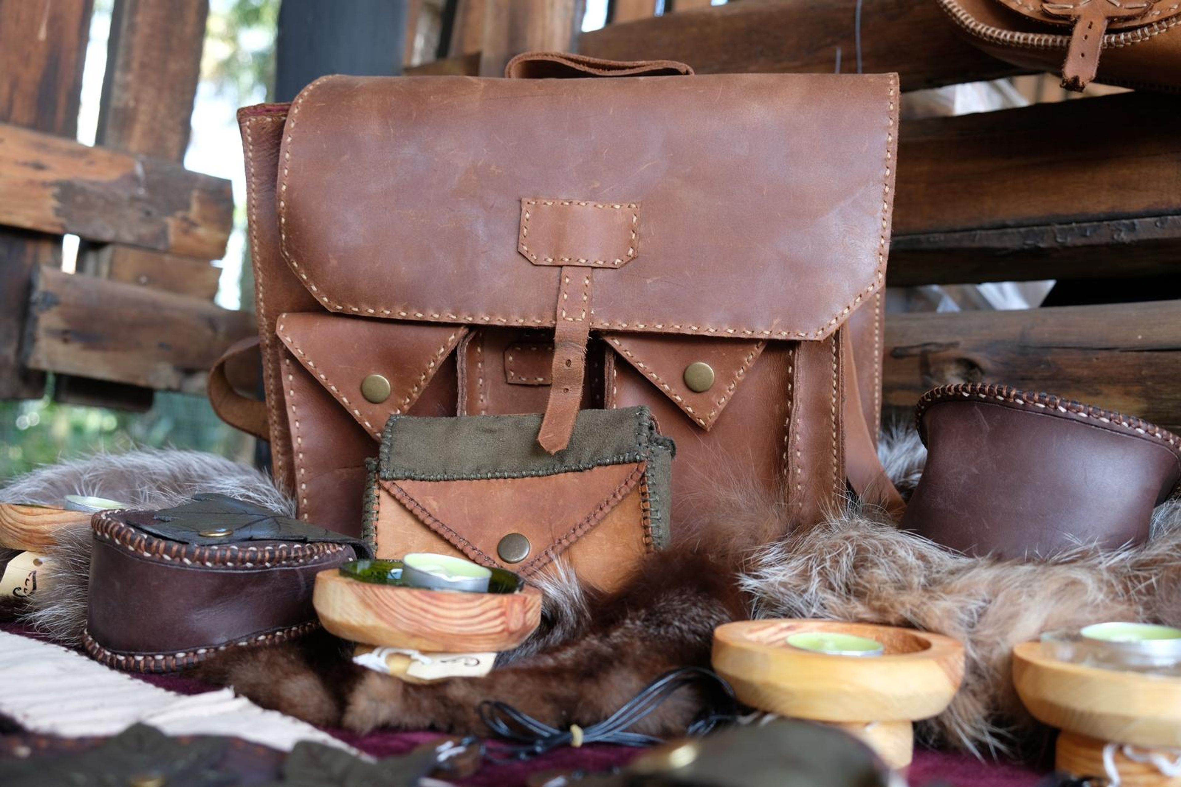 Handmade leather satchel with pouches and wooden bowls displayed on furs at the Juuks stall